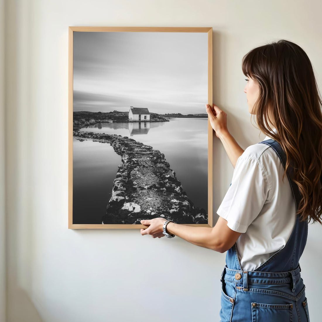Woman hanging a framed Connemara bothy photography print on a white wall.