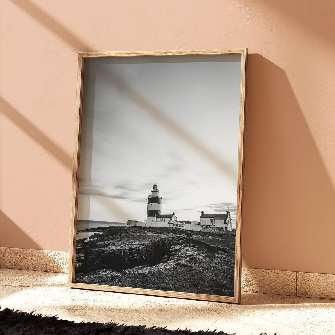 Framed lighthouse print against peach-toned wall with shadow