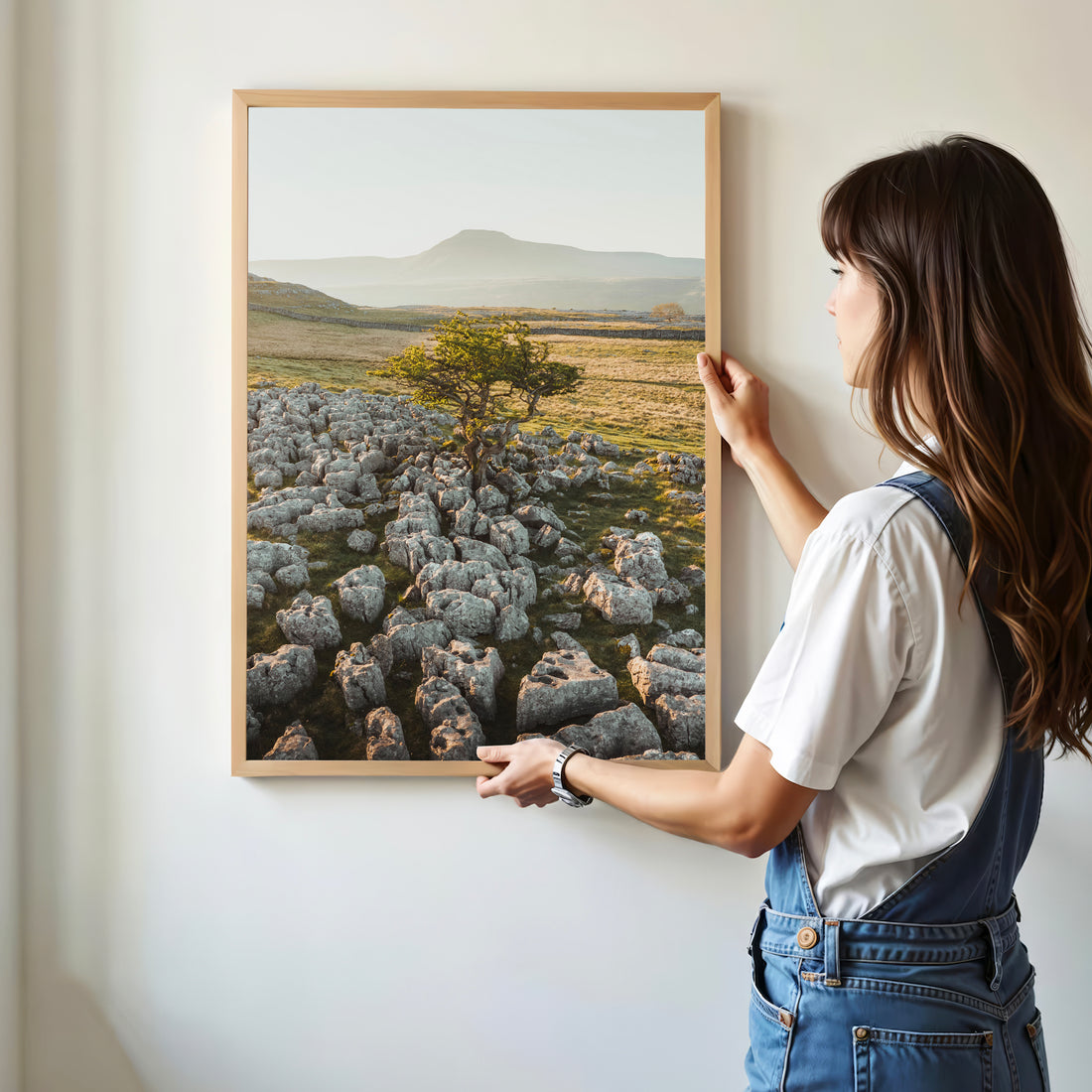 Woman hanging a Yorkshire Dales print of tree and limestone under soft light