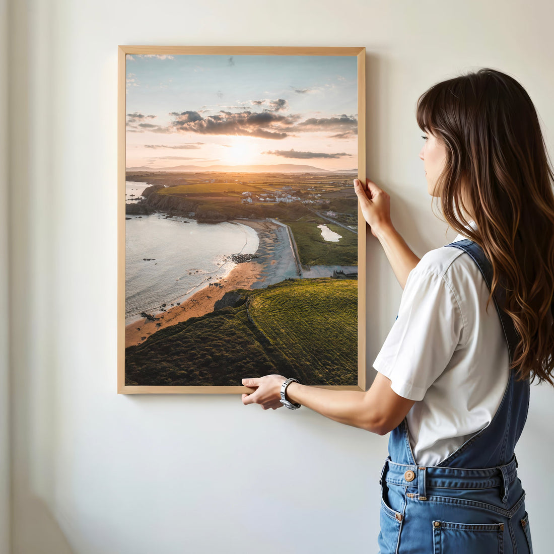 Woman hanging Annestown Beach sunset print on a white wall in soft daylight