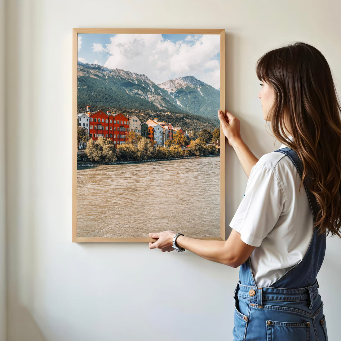 Framed Innsbruck mountain and river print leaning against wood wall in warm bedroom.