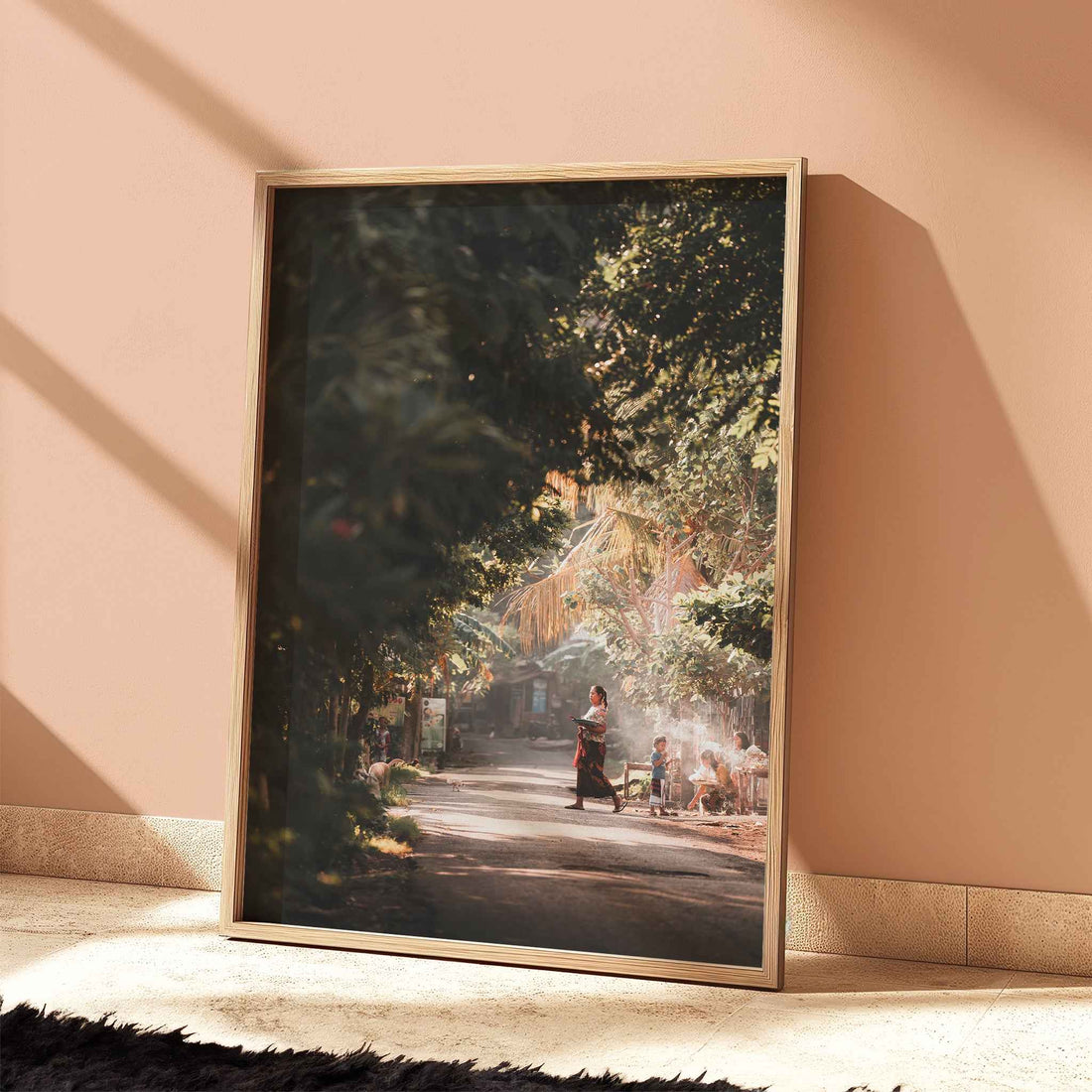 Bali village street photography large framed wall art print in natural wood frame leaning against white wall with dried flowers