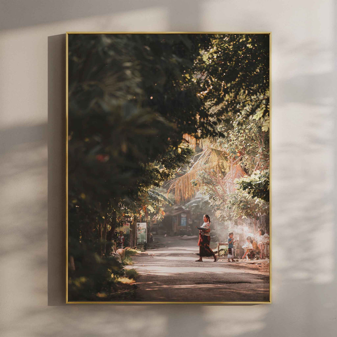 Bali village street photography wall art print with Balinese woman in traditional dress in gold floating frame mounted on beige wall with natural shadows
