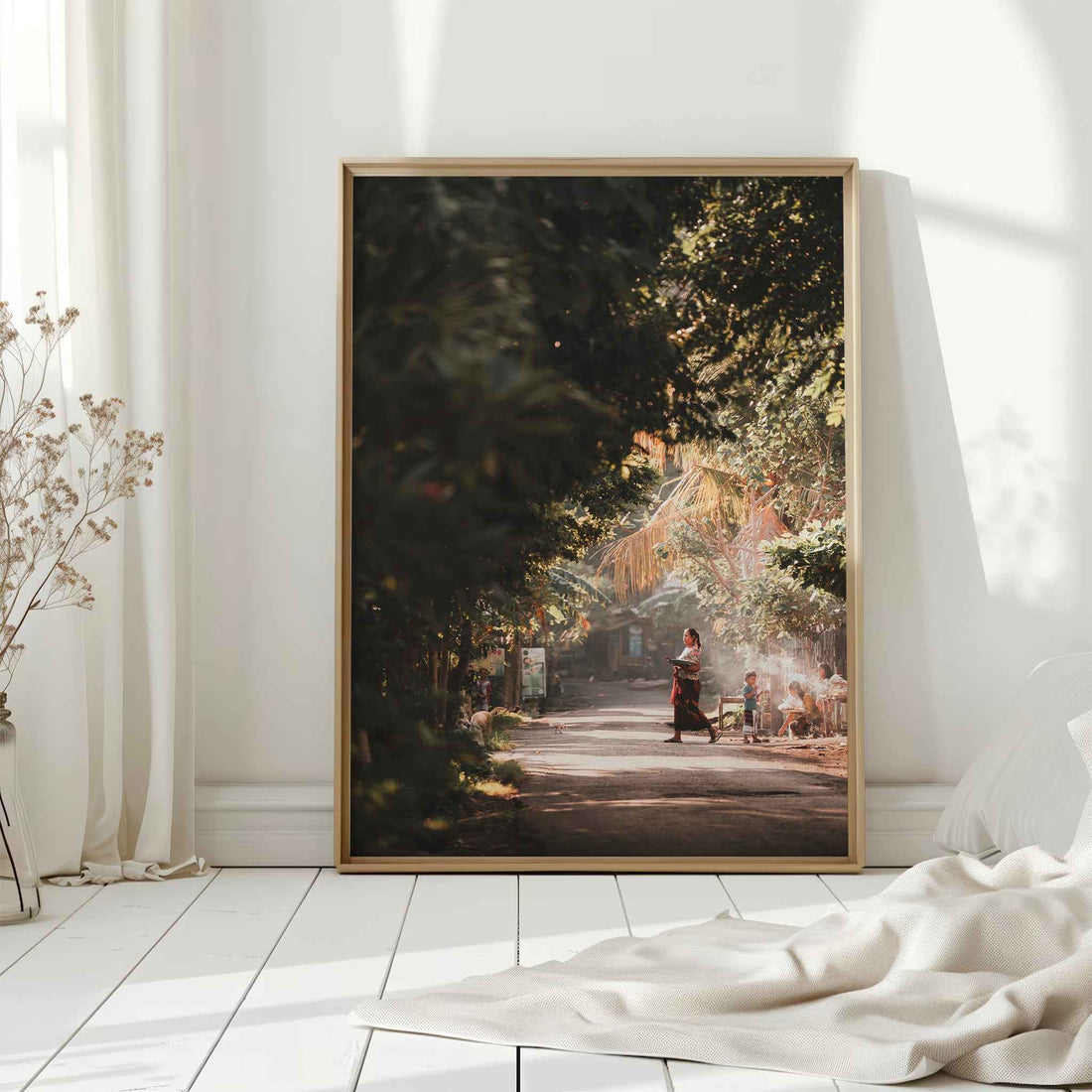 Bali village street photography large framed wall art print in natural wood frame leaning against white wall with dried flowers
