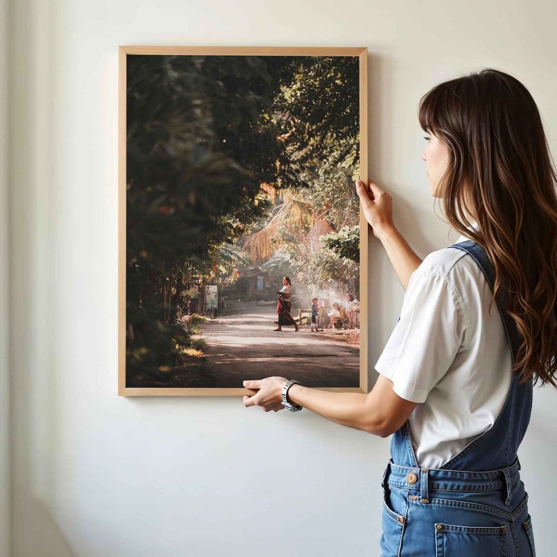Woman hanging Bali village street photography framed wall art print with golden jungle light in natural oak wood frame on white wall