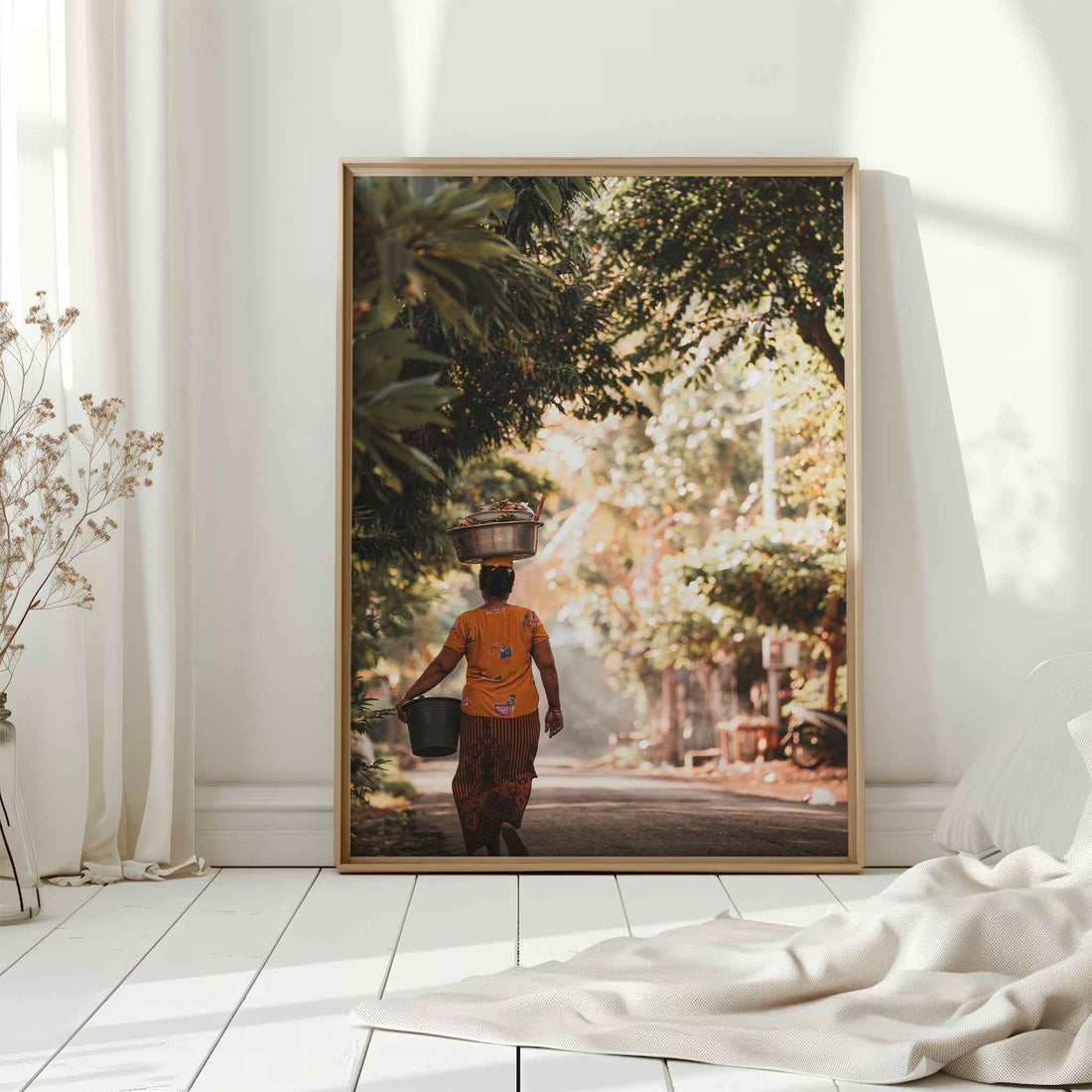 Balinese woman carrying offerings large framed wall art print in natural wood frame leaning against white wall with dried flowers
