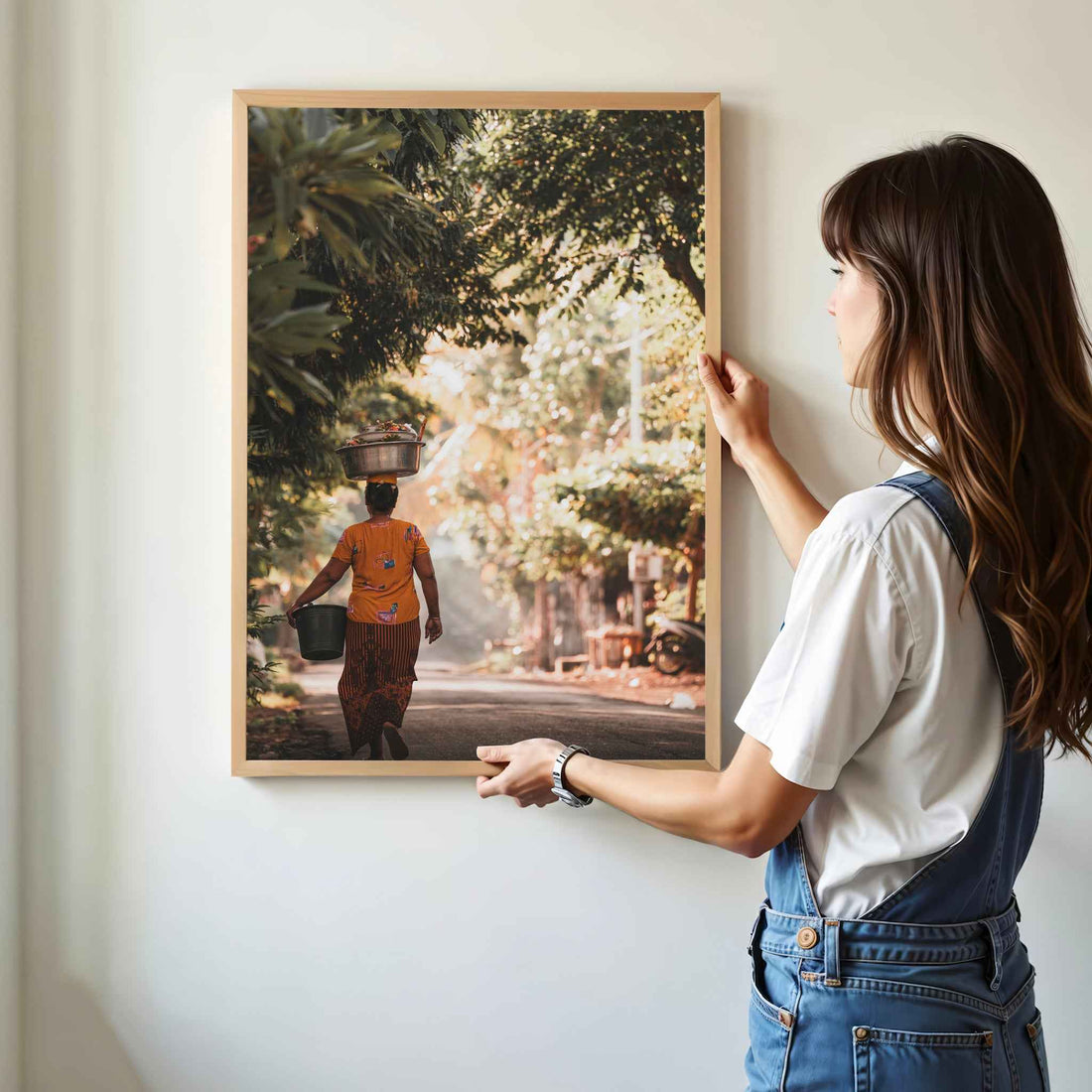 Woman hanging Balinese woman carrying offerings framed wall art print with golden jungle light in natural oak wood frame on white wall
