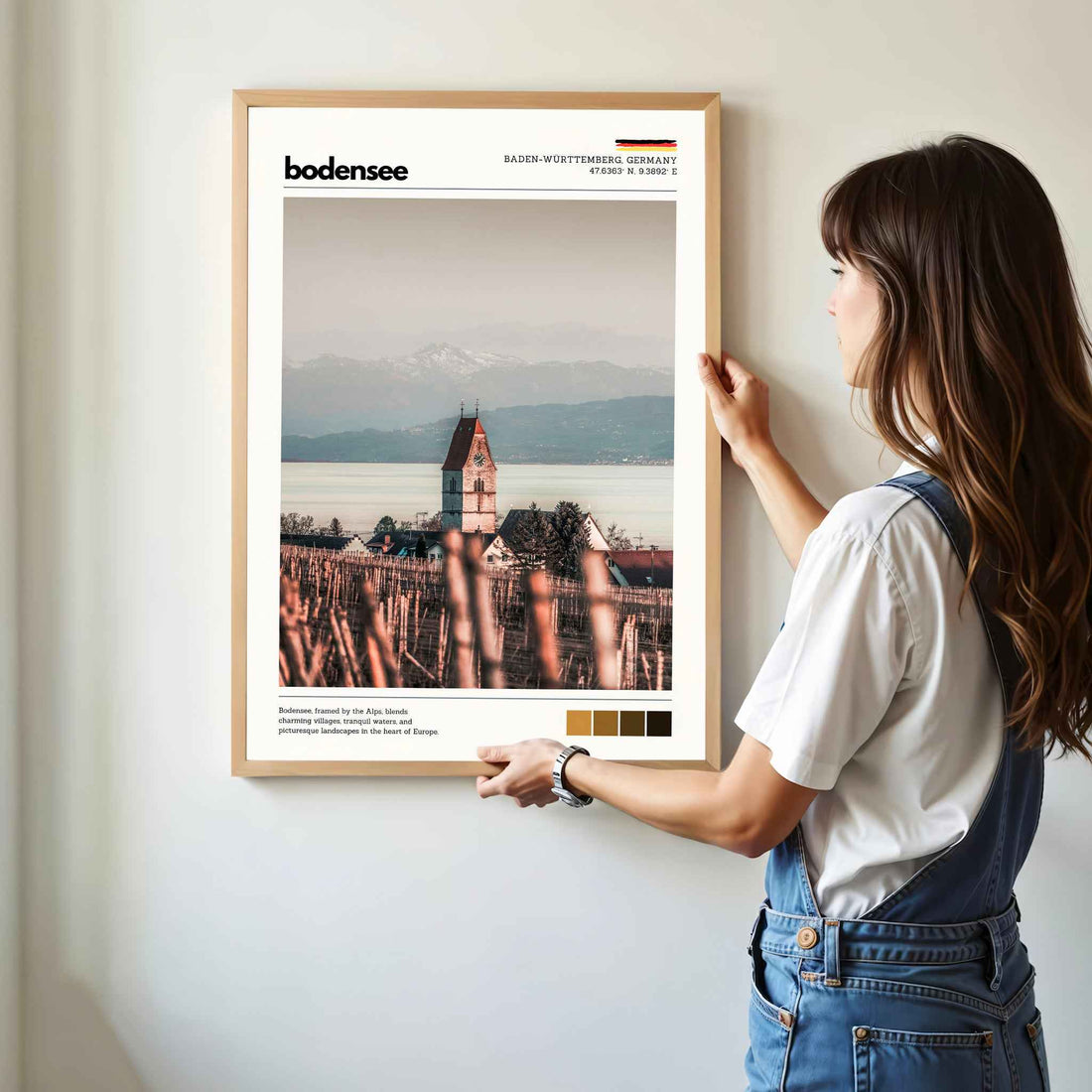 Woman hanging framed Bodensee Lake Constance Germany church and vineyard photography print in natural oak frame on white wall