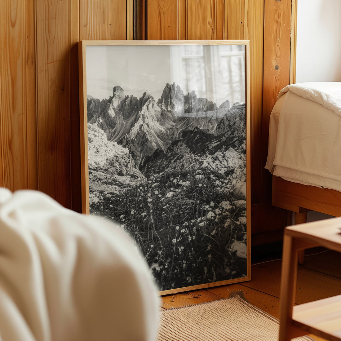 Black and white mountain print of Cadini di Misurina resting against a pine wood wall in a cosy bedroom.