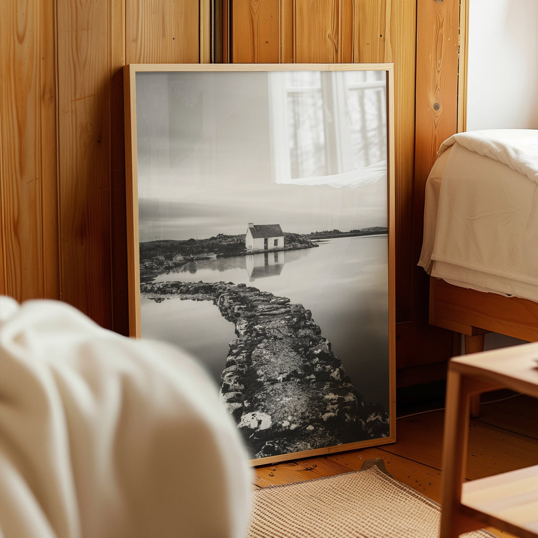 Framed black and white Irish landscape print resting by a wooden bed.
