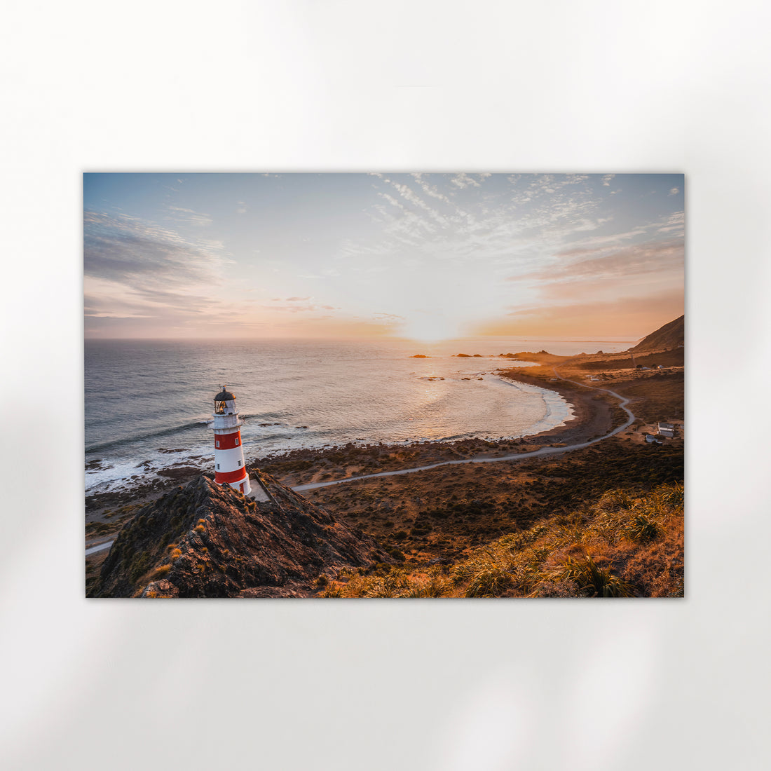 Unframed Cape Palliser lighthouse landscape fine art print on white background showing red and white striped lighthouse at golden hour over curved coastline