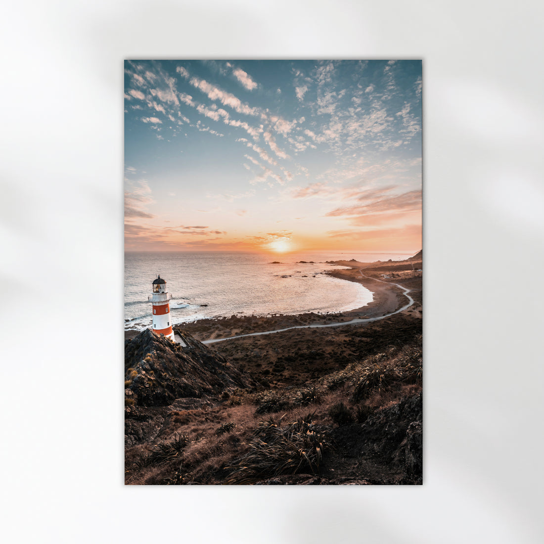 Unframed Cape Palliser lighthouse fine art print on white background showing red and white striped lighthouse at sunset over curved coastline