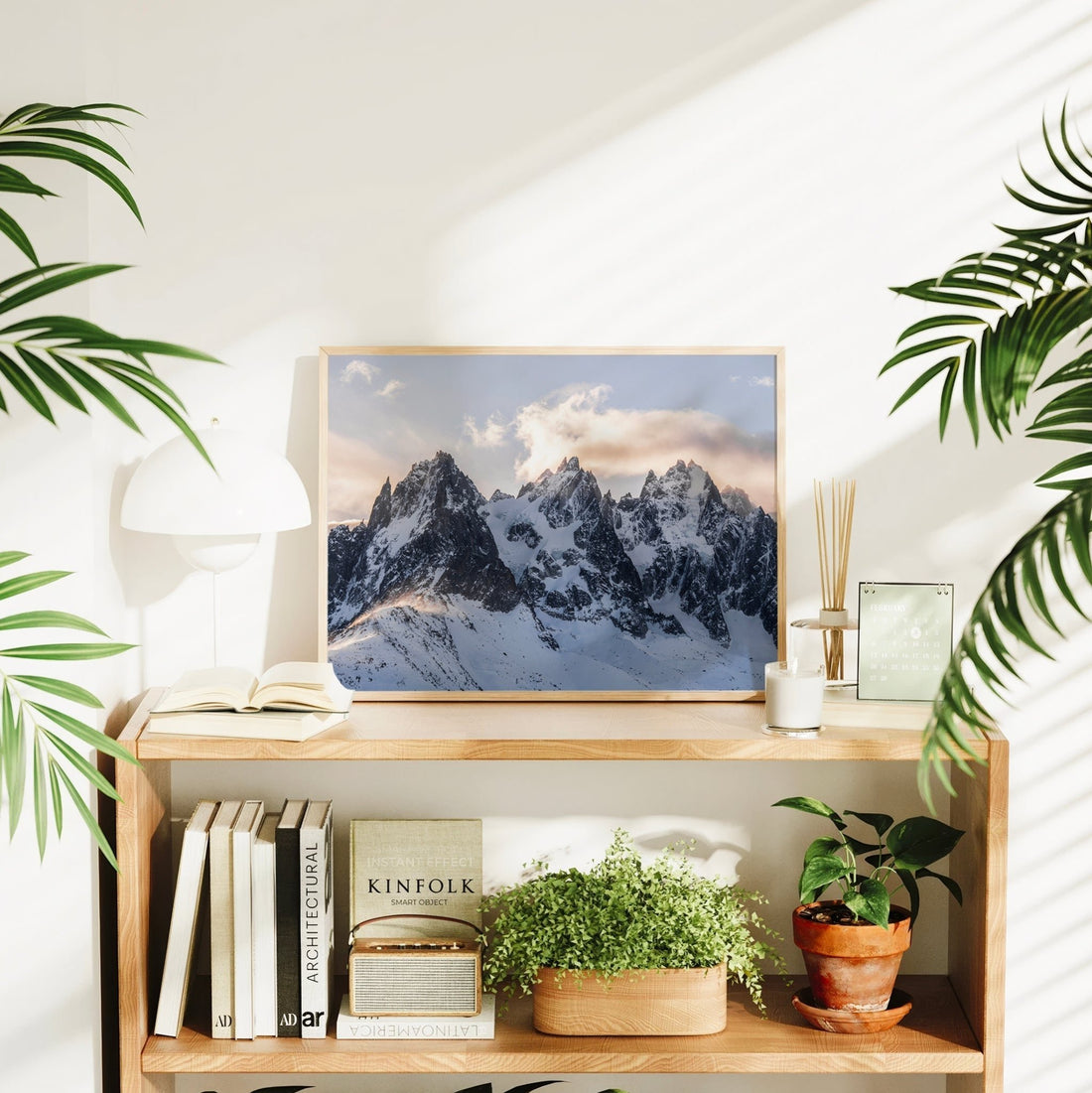 Sunset-lit alpine print of jagged snowy peaks above bookshelf and plants
