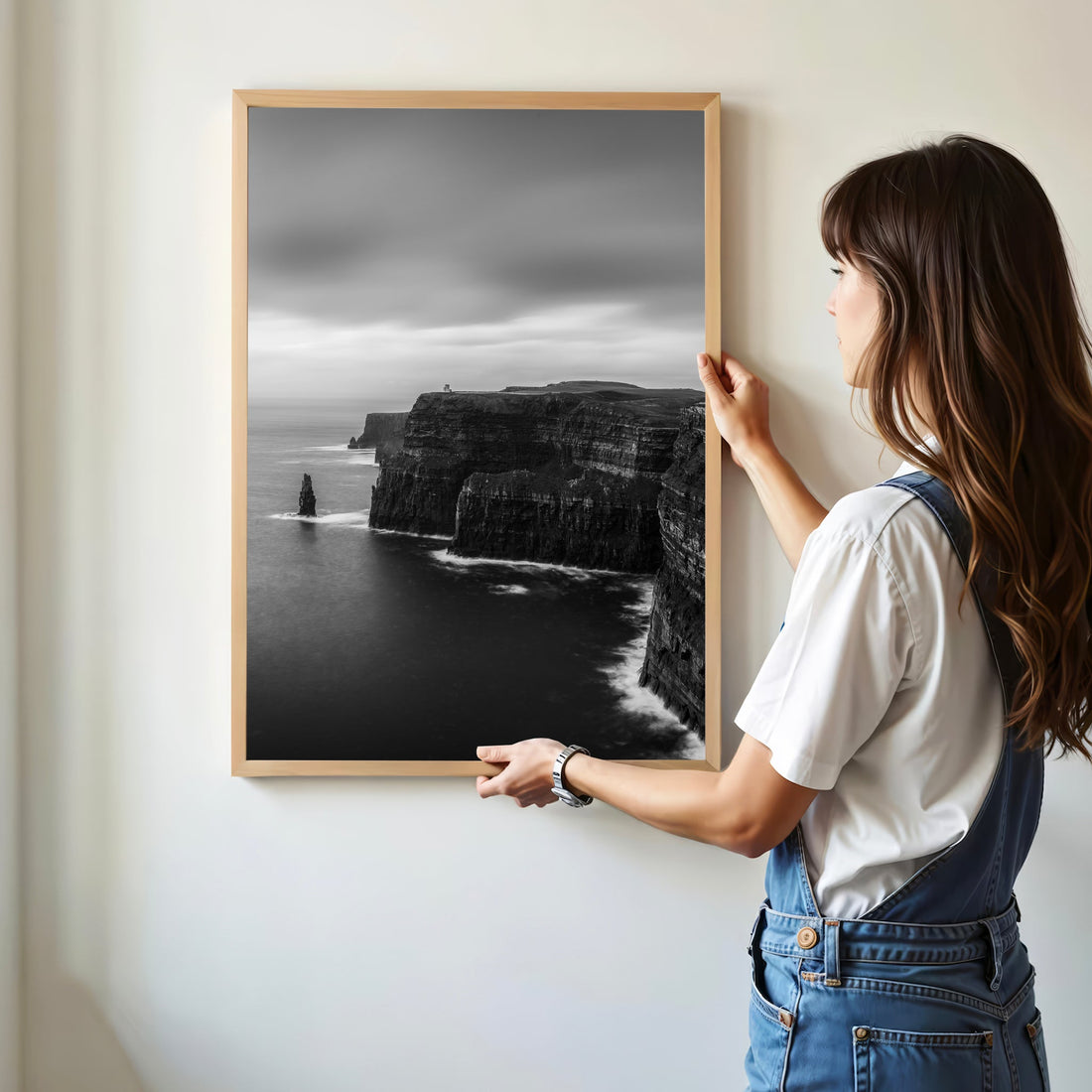 Woman hanging framed black and white print of the Cliffs of Moher in minimalist room