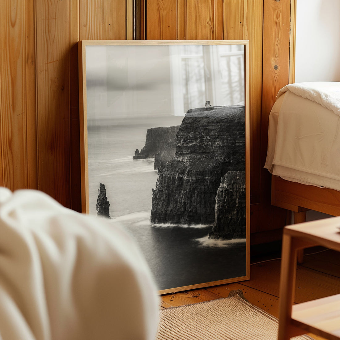 Framed black and white Cliffs of Moher print resting on floor in wood-panelled bedroom