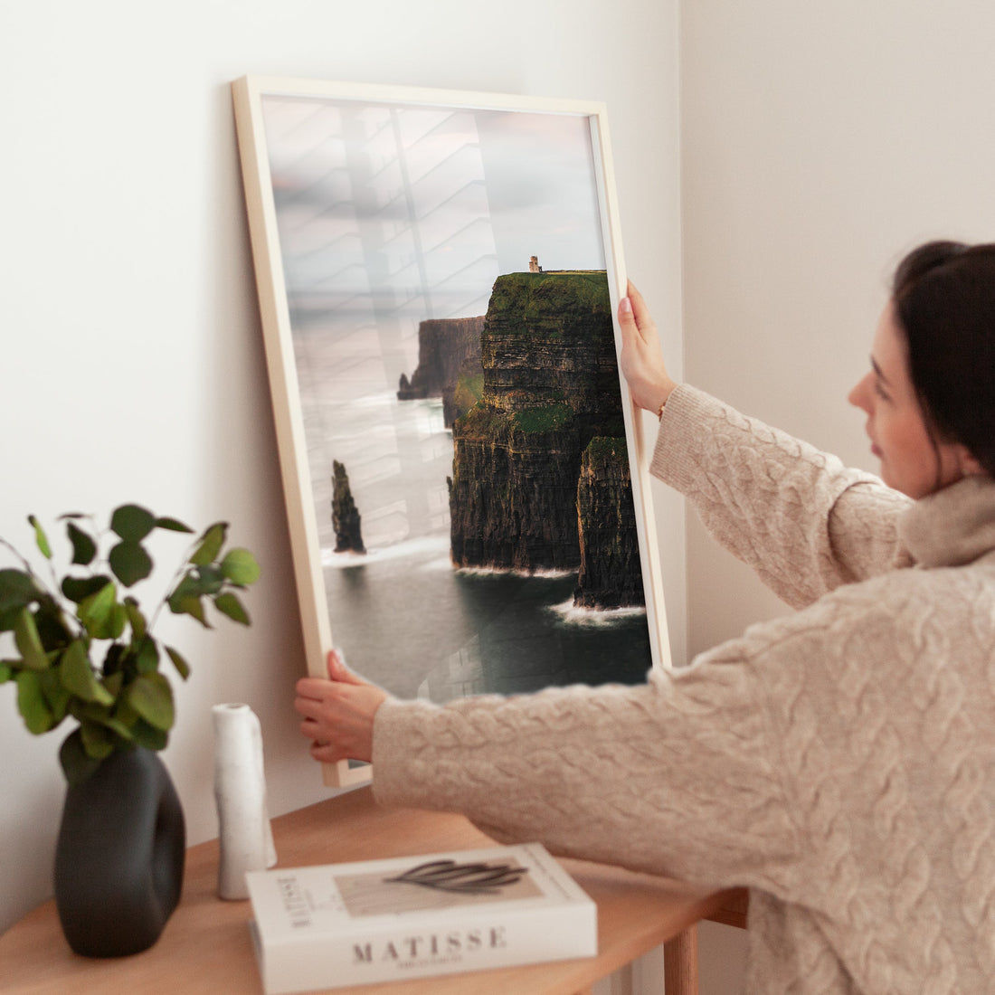 Framed Irish landscape print of Cliffs of Moher being placed on a modern wooden table