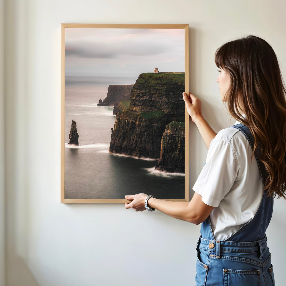 Woman hanging a Cliffs of Moher landscape print in a minimalist modern home