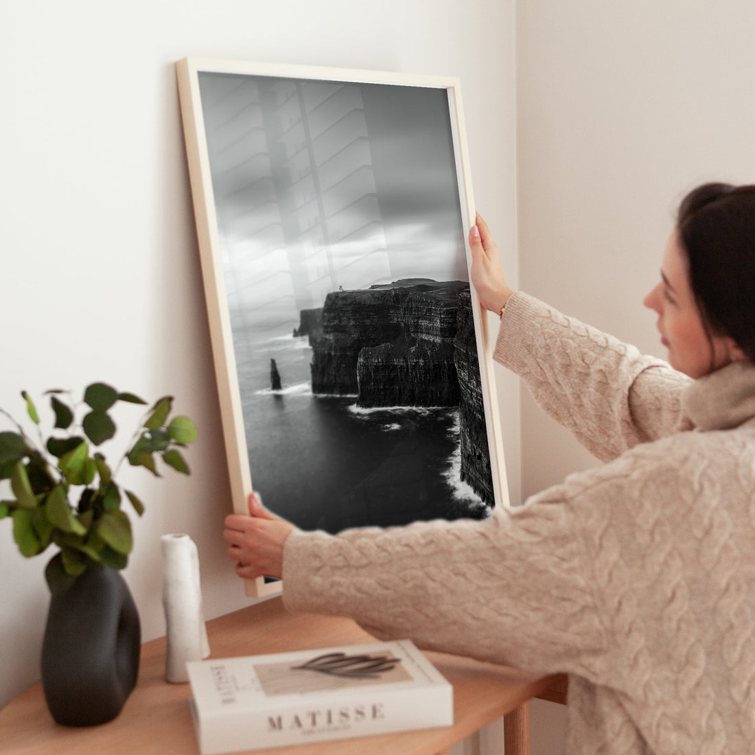 Woman adjusting framed black and white Cliffs of Moher print on wooden side table