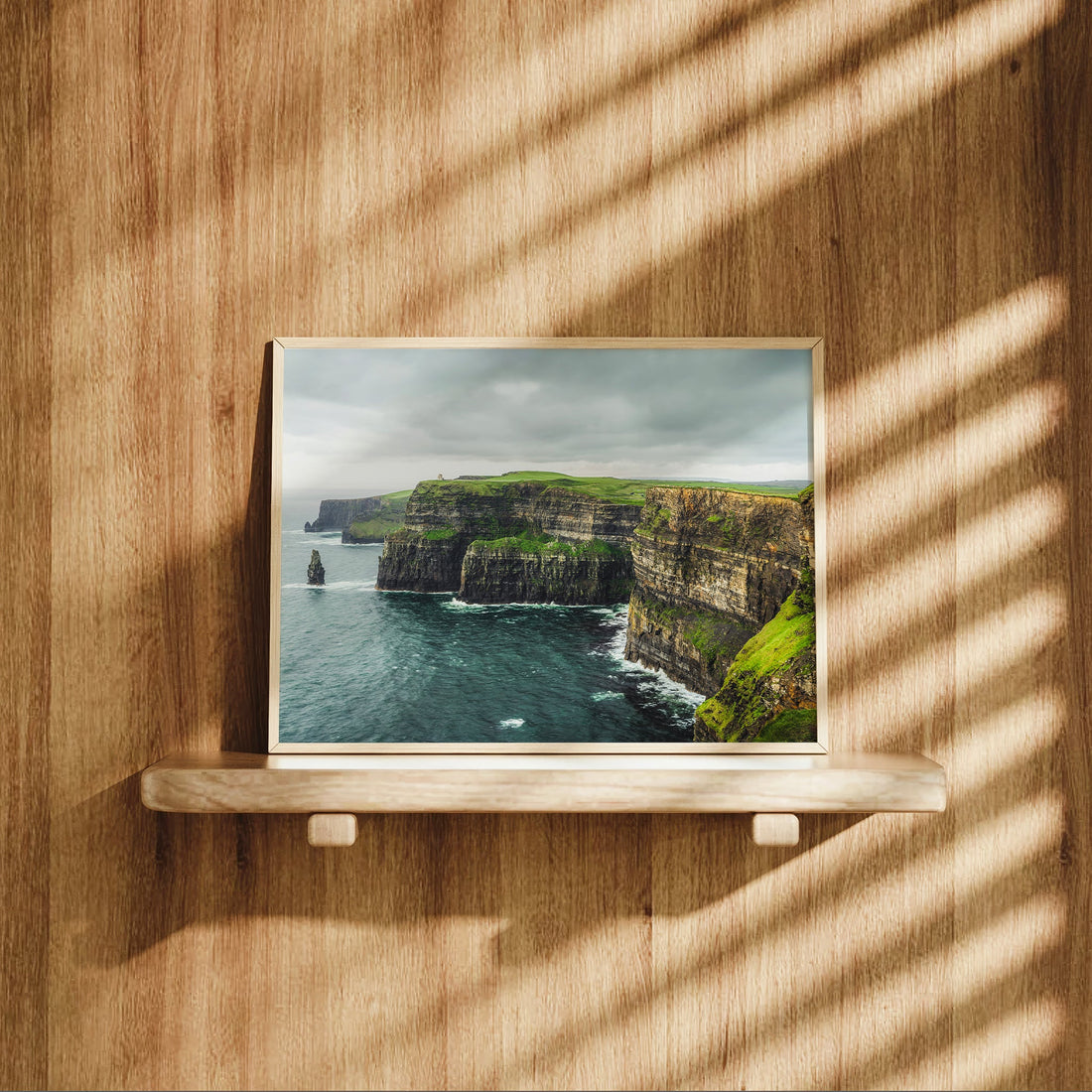Irish coastal landscape print on a wooden shelf with sunlight casting striped shadows