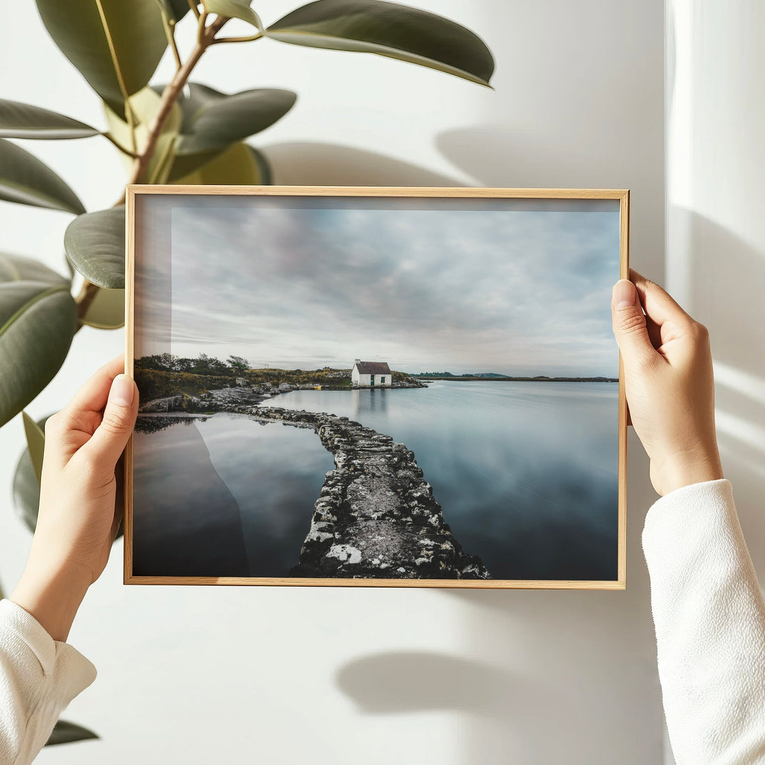 A person holding a framed print of a Connemara fisherman's bothy in daylight.