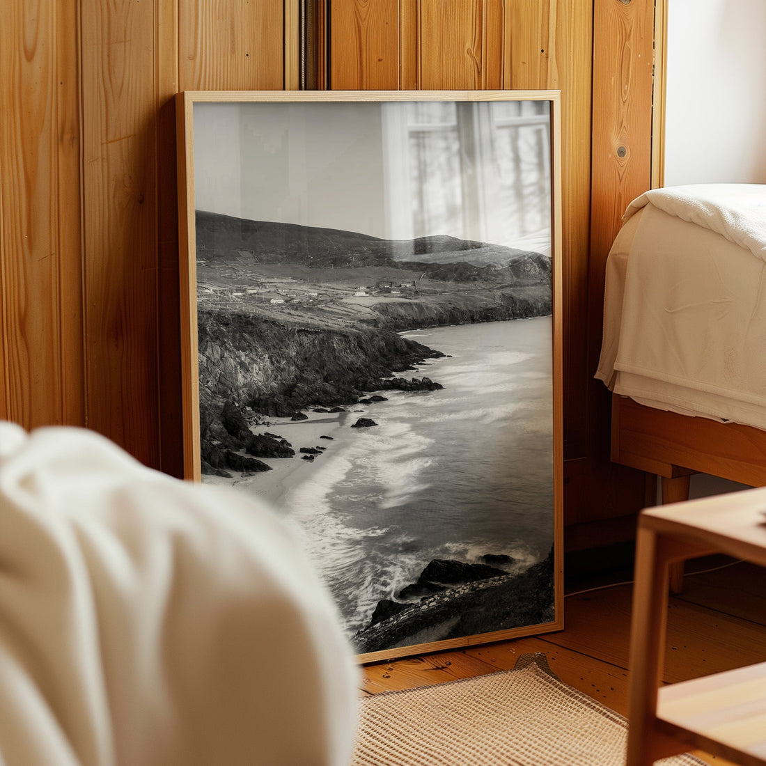 Framed black and white Coumeenoole Beach artwork leaning against wooden bedroom wall