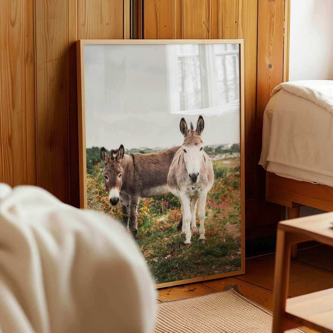 Rustic print of two donkeys beside a bed in a timber cottage room.