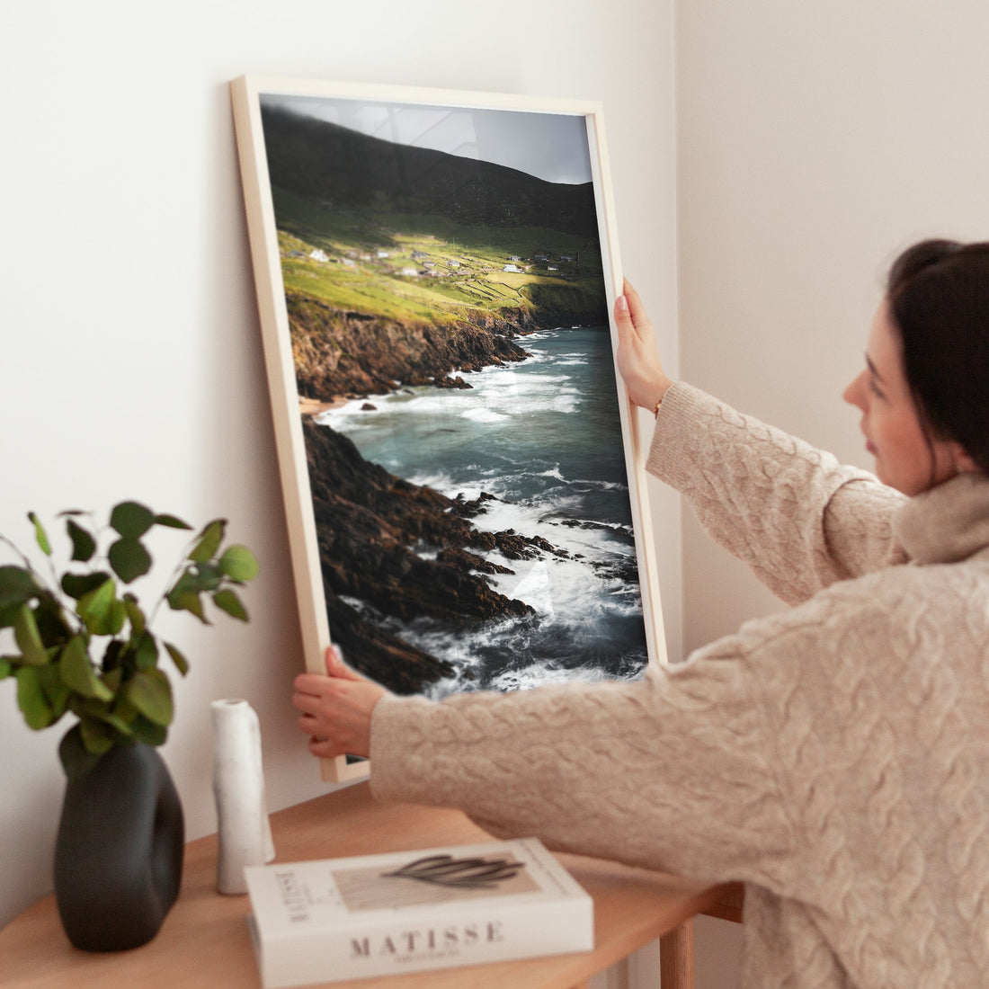 Woman adjusting framed Coumeenoole Beach photo print in a minimal room.
