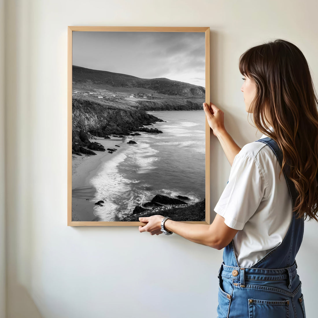 Woman hanging framed black and white Coumeenoole Beach print in modern room