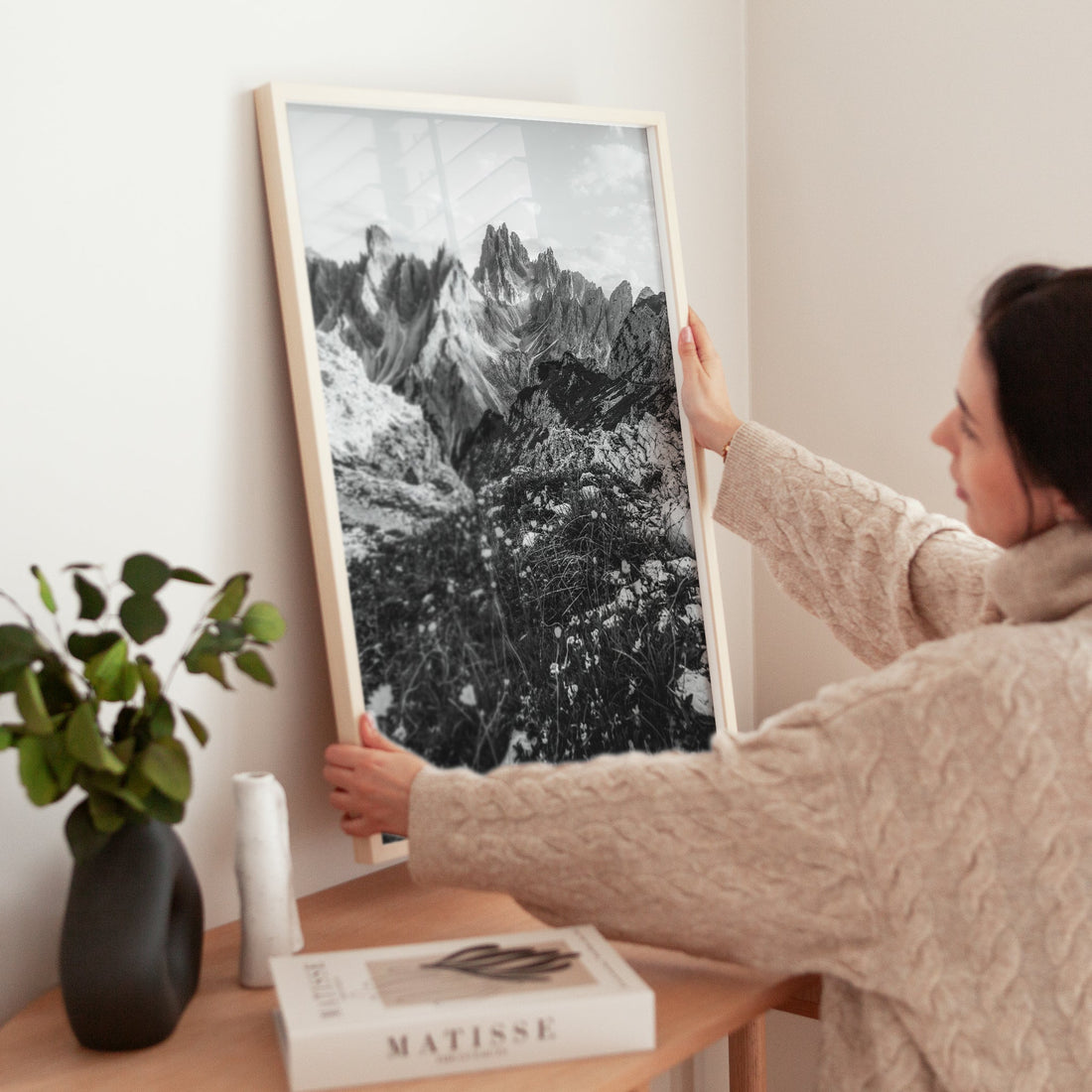 Woman styling a fine art mountain print of Cadini di Misurina on a wooden side table.
