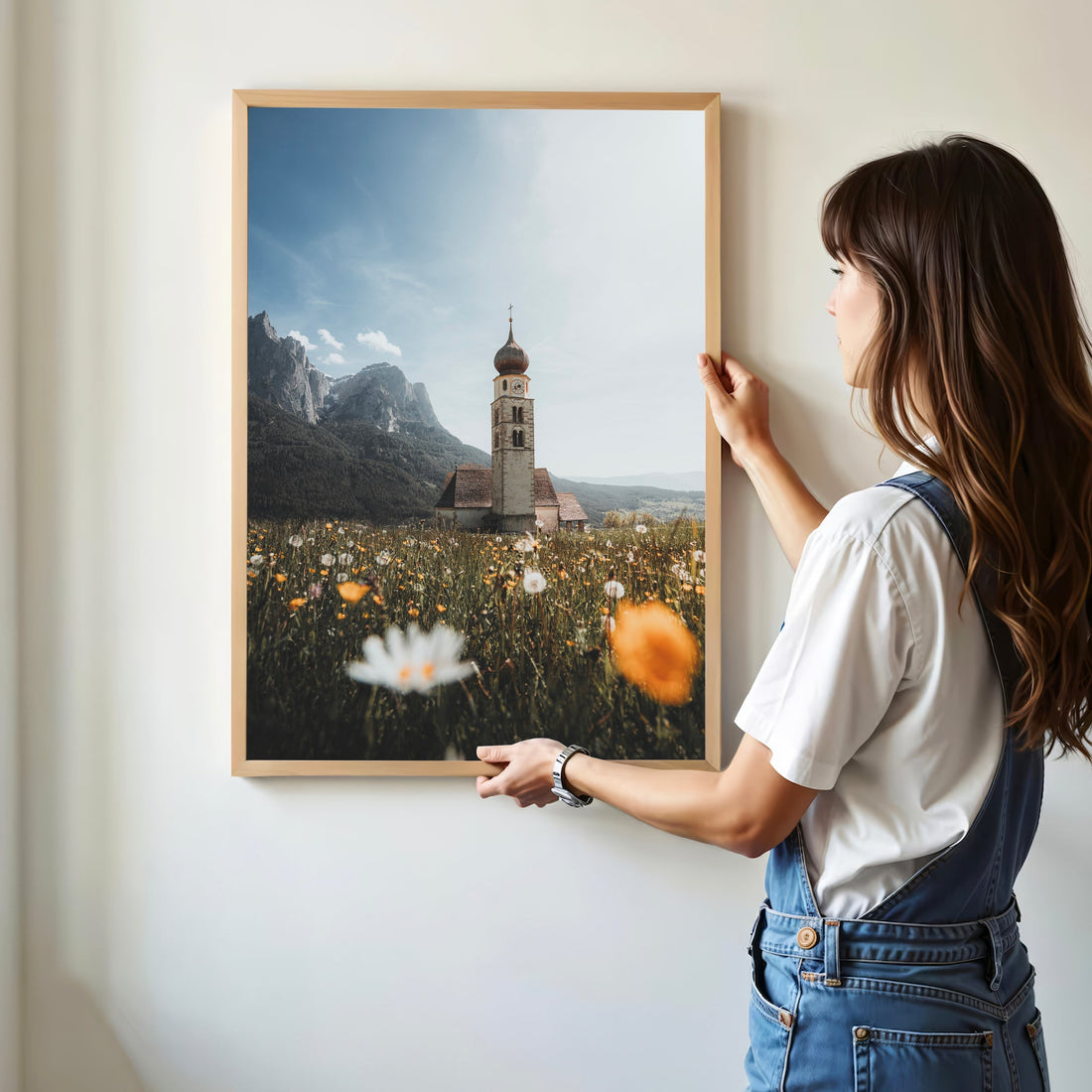 Woman hanging a framed poster of San Valentino church in a wildflower field