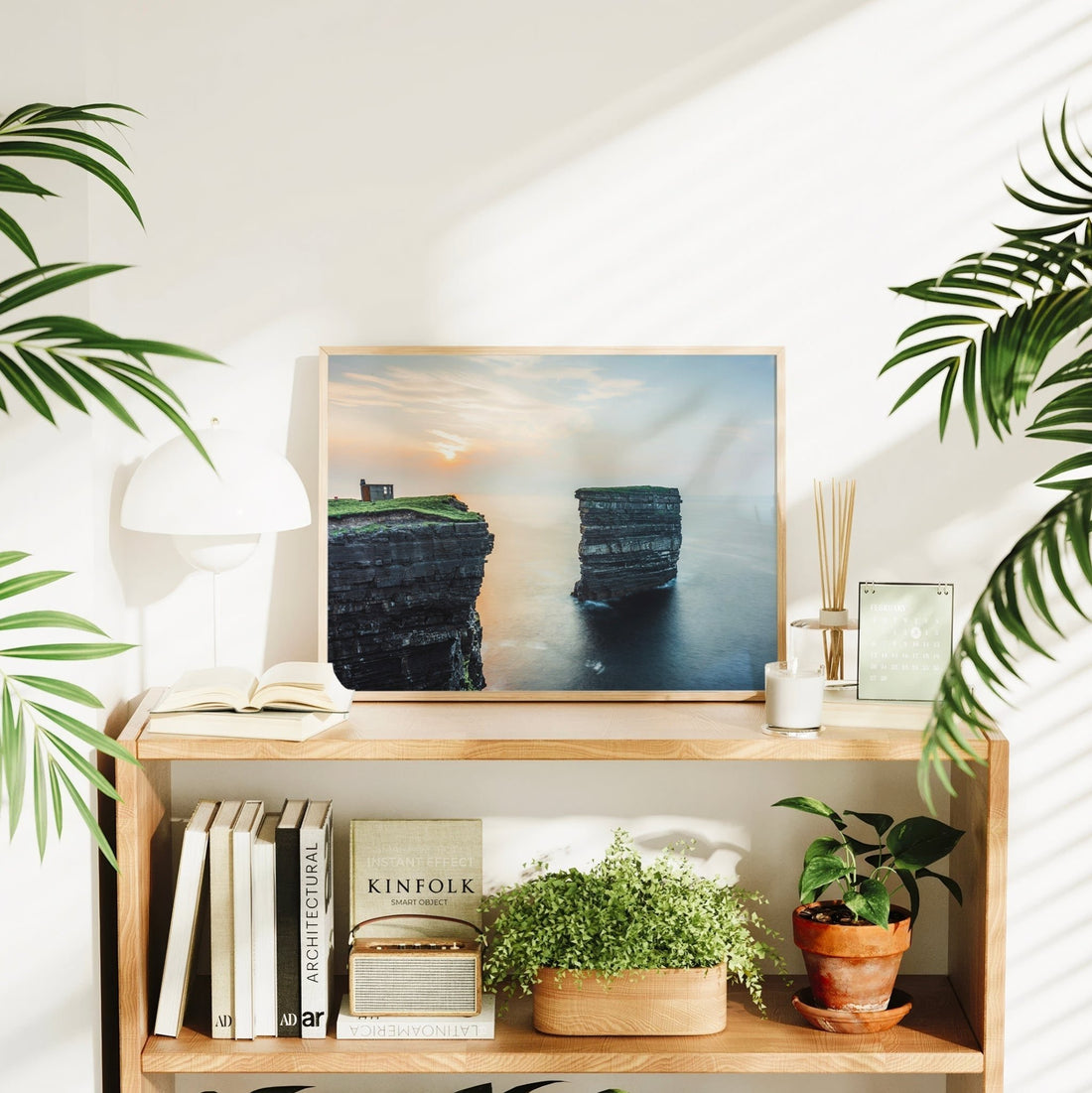 Framed Downpatrick Head wall art styled on bookshelf with plants and sunset glow