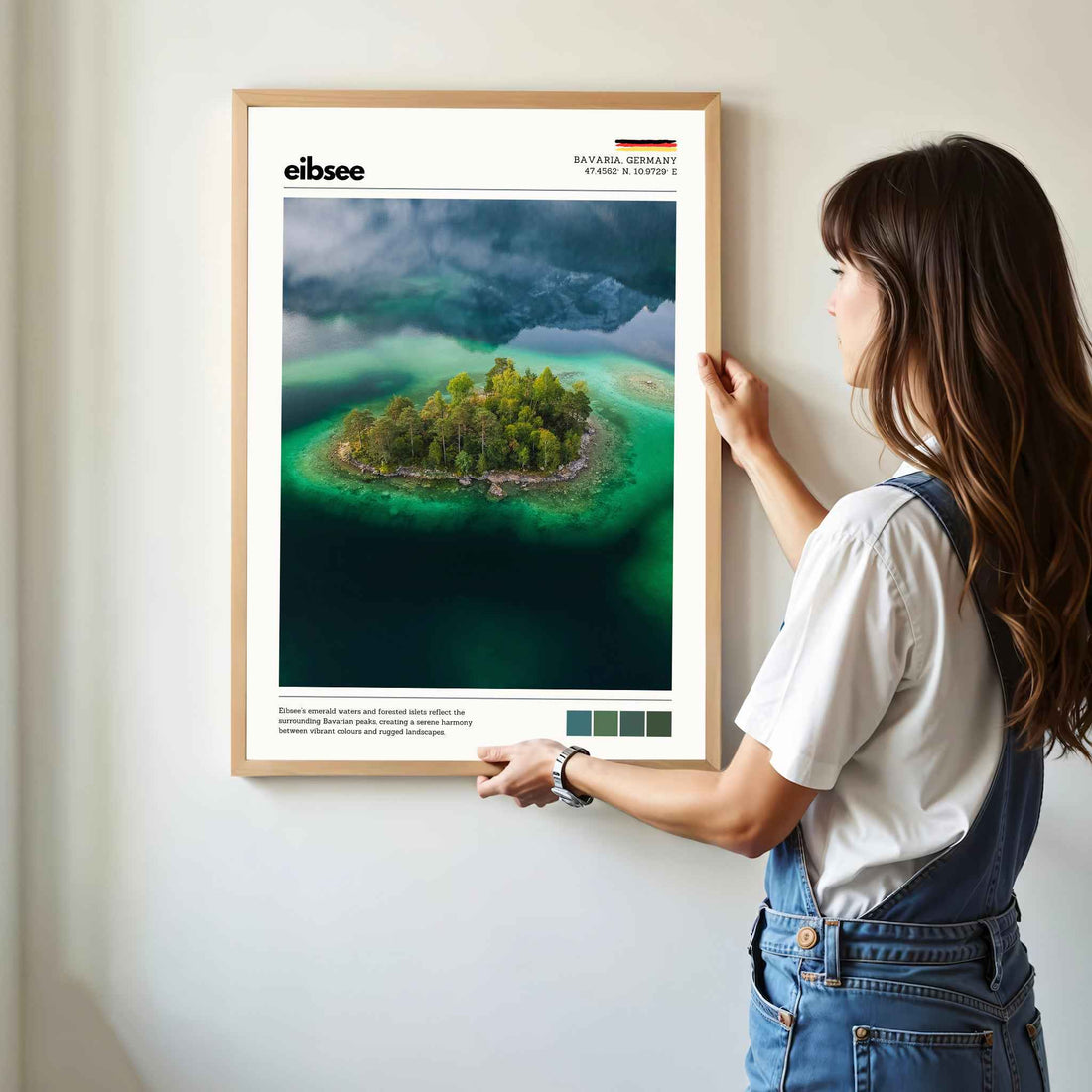 Woman hanging framed Eibsee aerial island Bavaria Germany drone photography print in natural oak frame on white wall