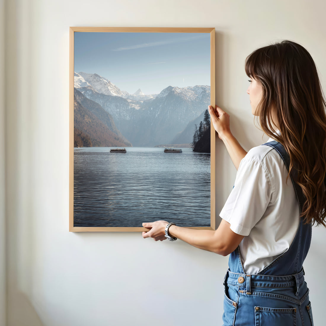Woman hanging framed Königssee mountain lake print on white wall