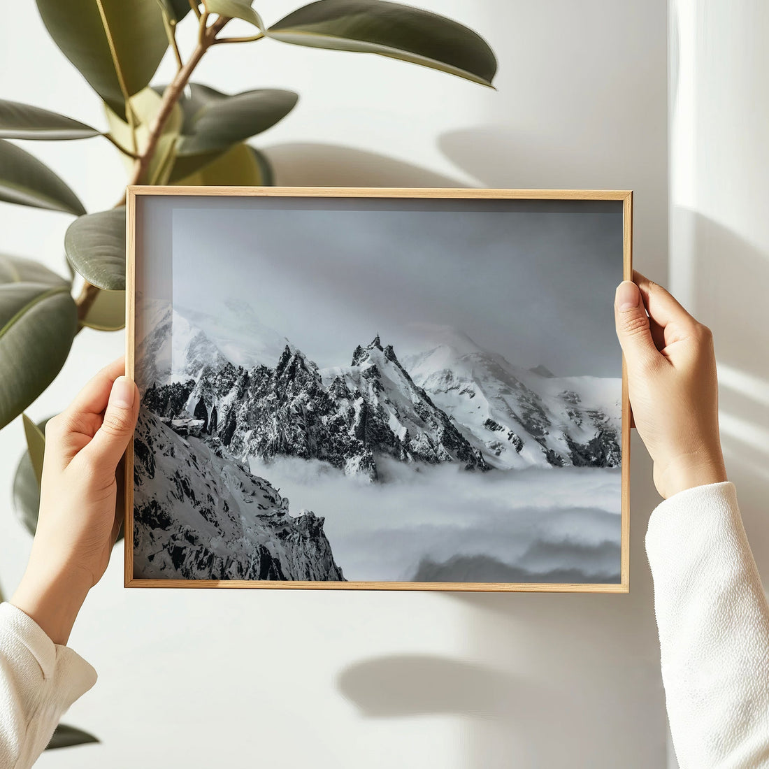 A person holding a framed Aiguille du Midi print with snowy mountains in view