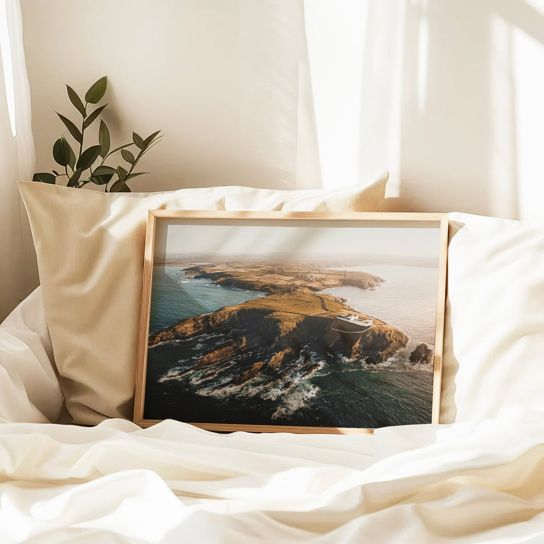 Framed lighthouse art resting on a cream duvet in soft sunlight
