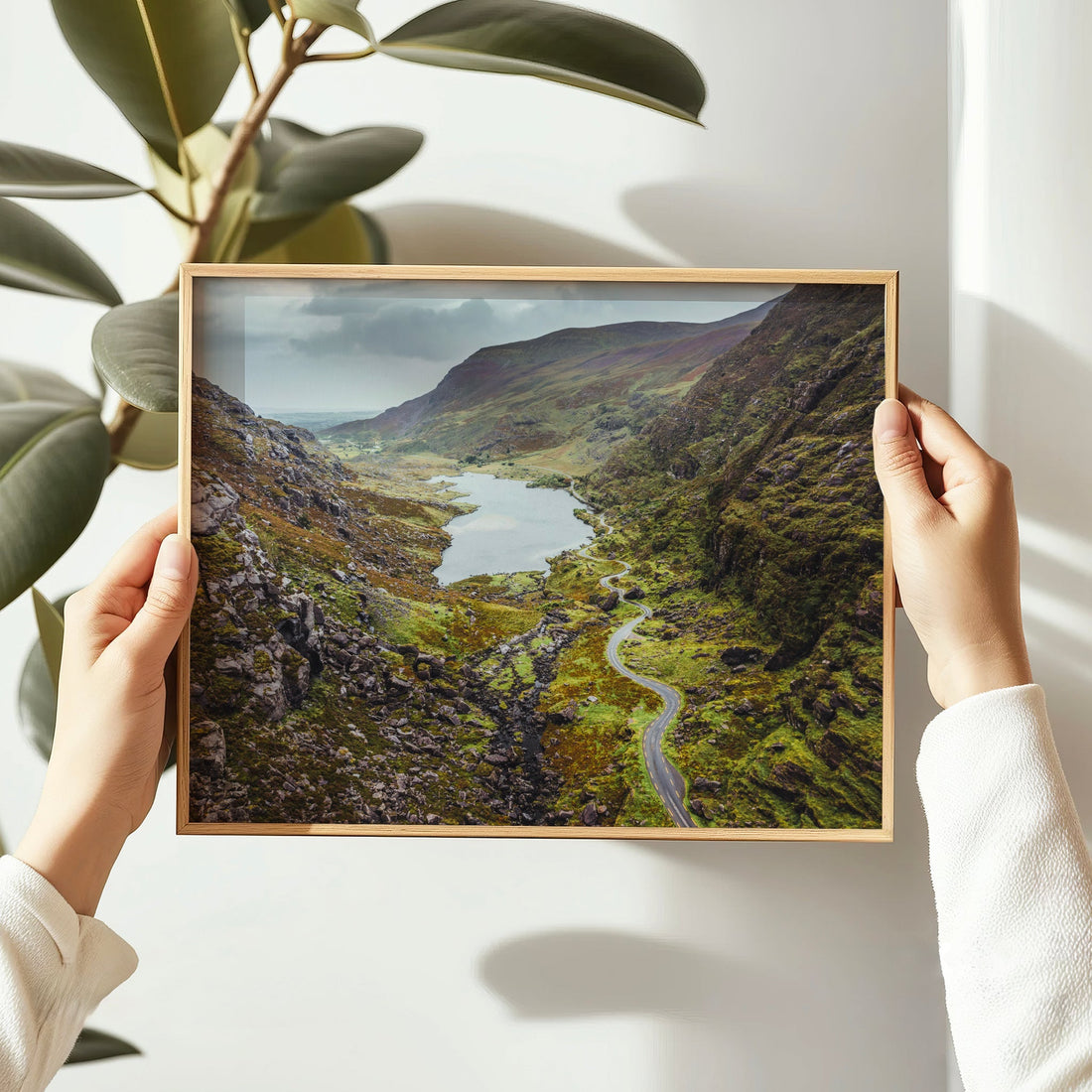 Hands holding a wooden-framed photo print of the Gap of Dunloe, with soft natural lighting.