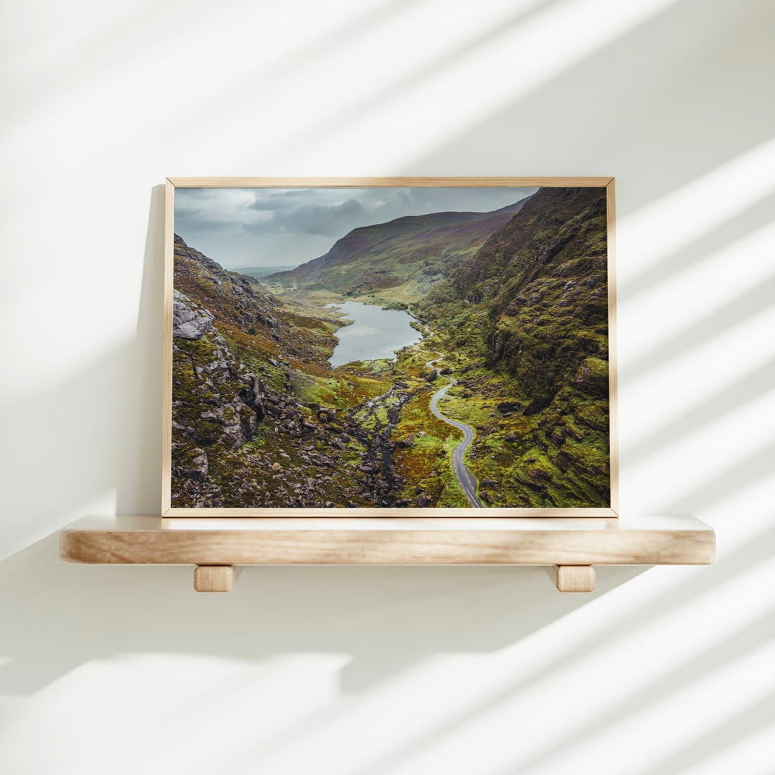 Brightly lit shelf displaying framed artwork of the Gap of Dunloe, with deep green and earthy tones.