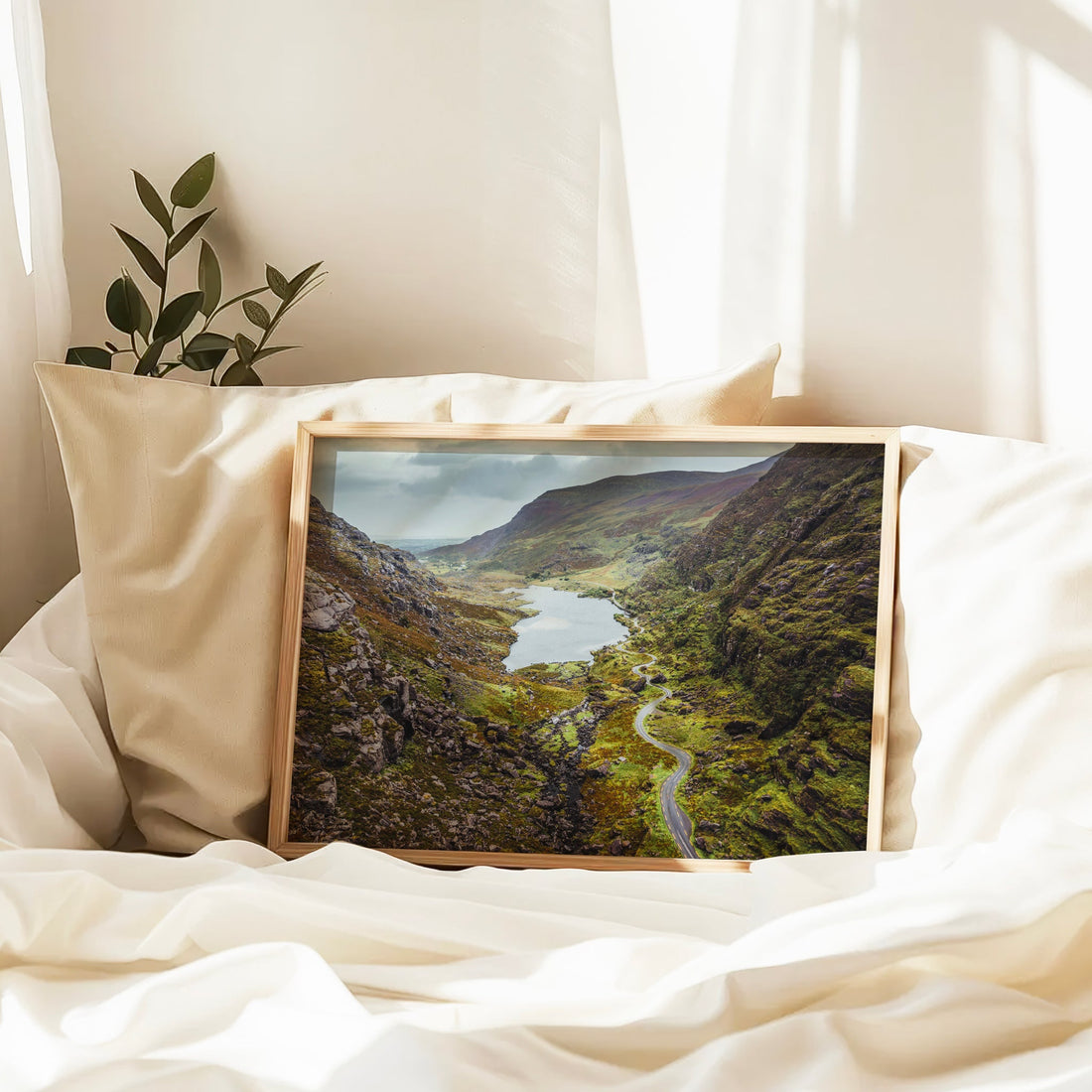 Gap of Dunloe wall print resting on a bed with cream sheets, highlighting the winding valley road.