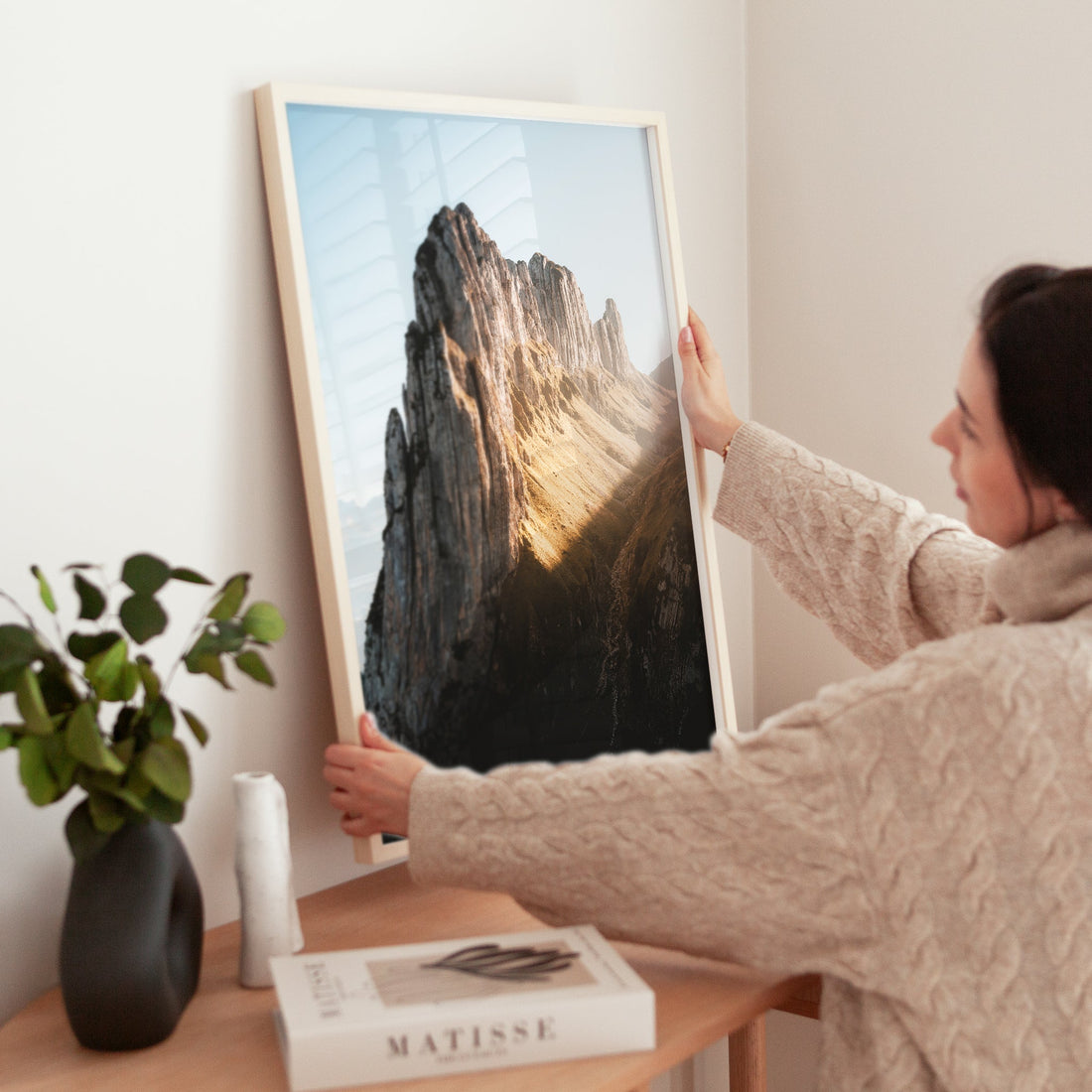 Close-up of a framed Saxer Lücke Swiss Alps photo being placed on a modern interior shelf.