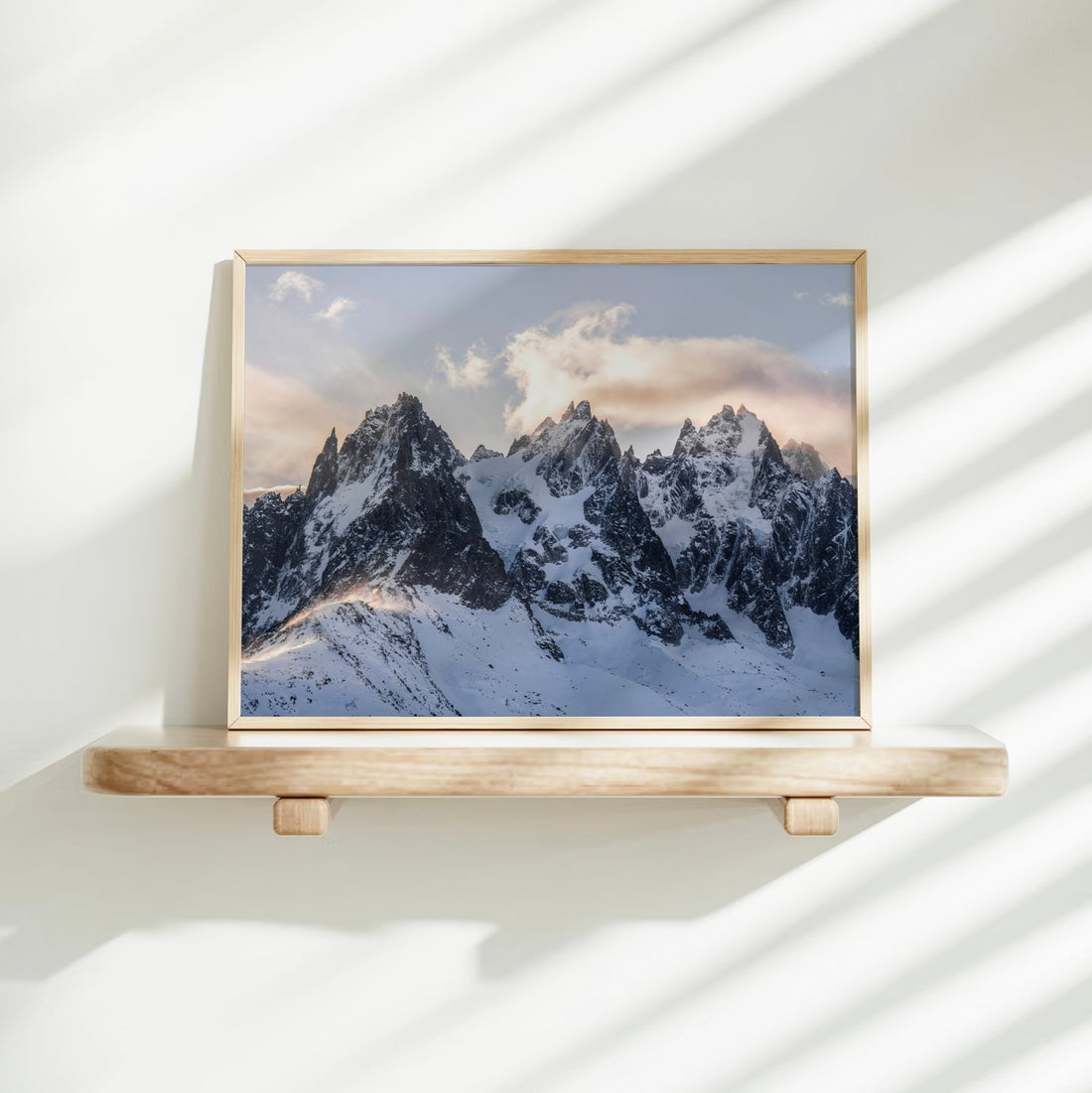 Soft golden light on dramatic alpine ridge print styled on floating shelf
