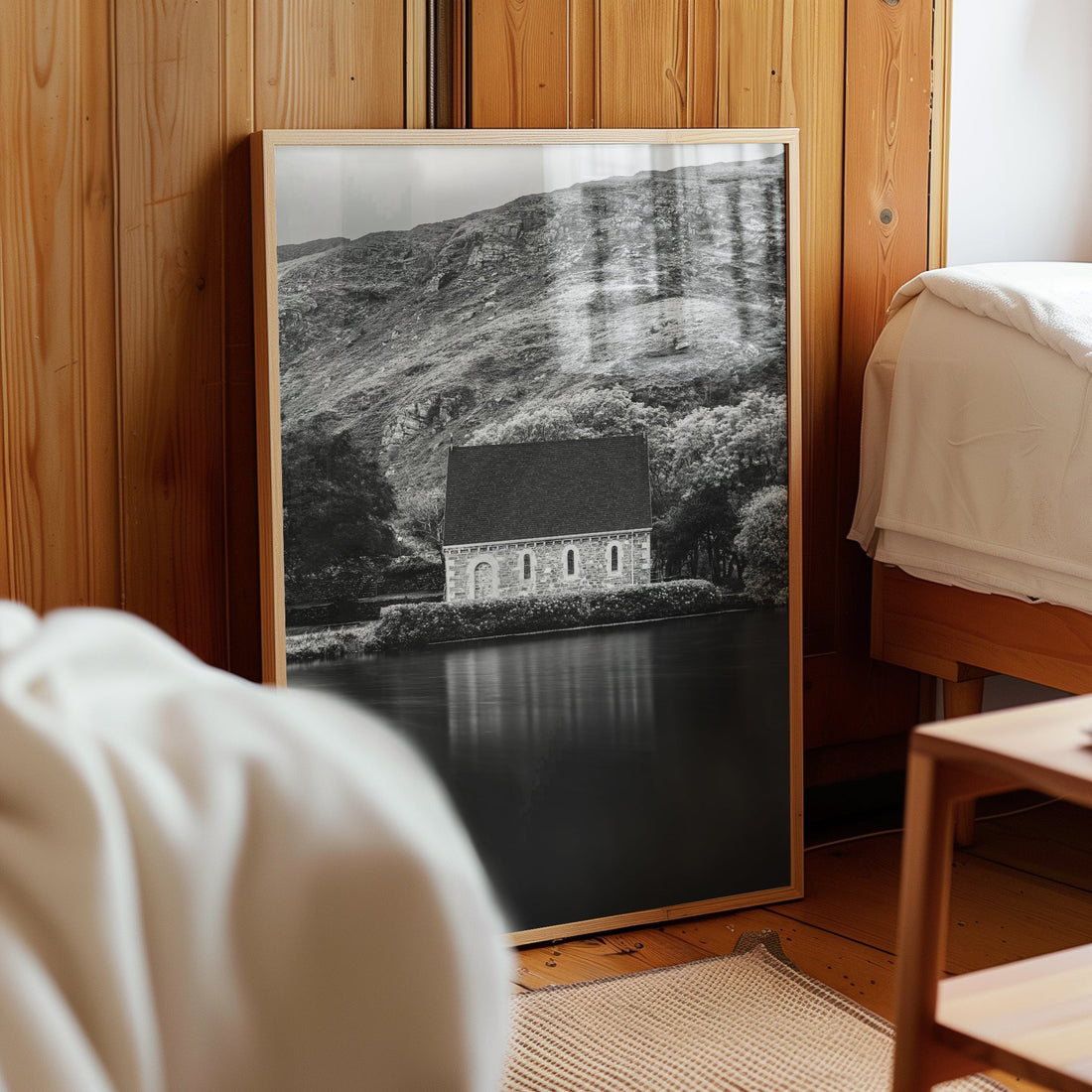 Framed Gougane Barra chapel print leaning against wooden bedroom wall
