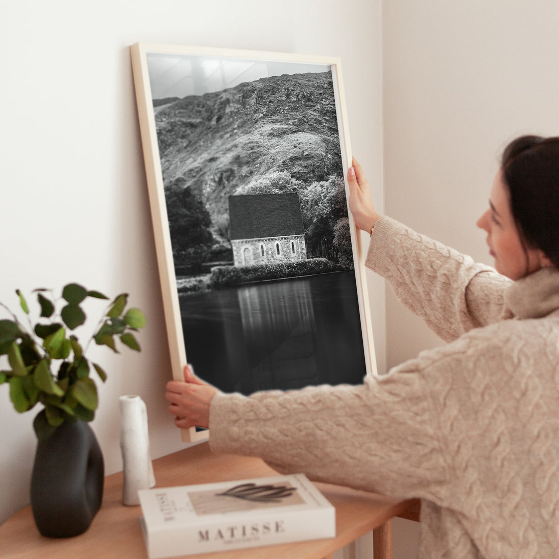 Woman placing Gougane Barra chapel art print on minimalist table