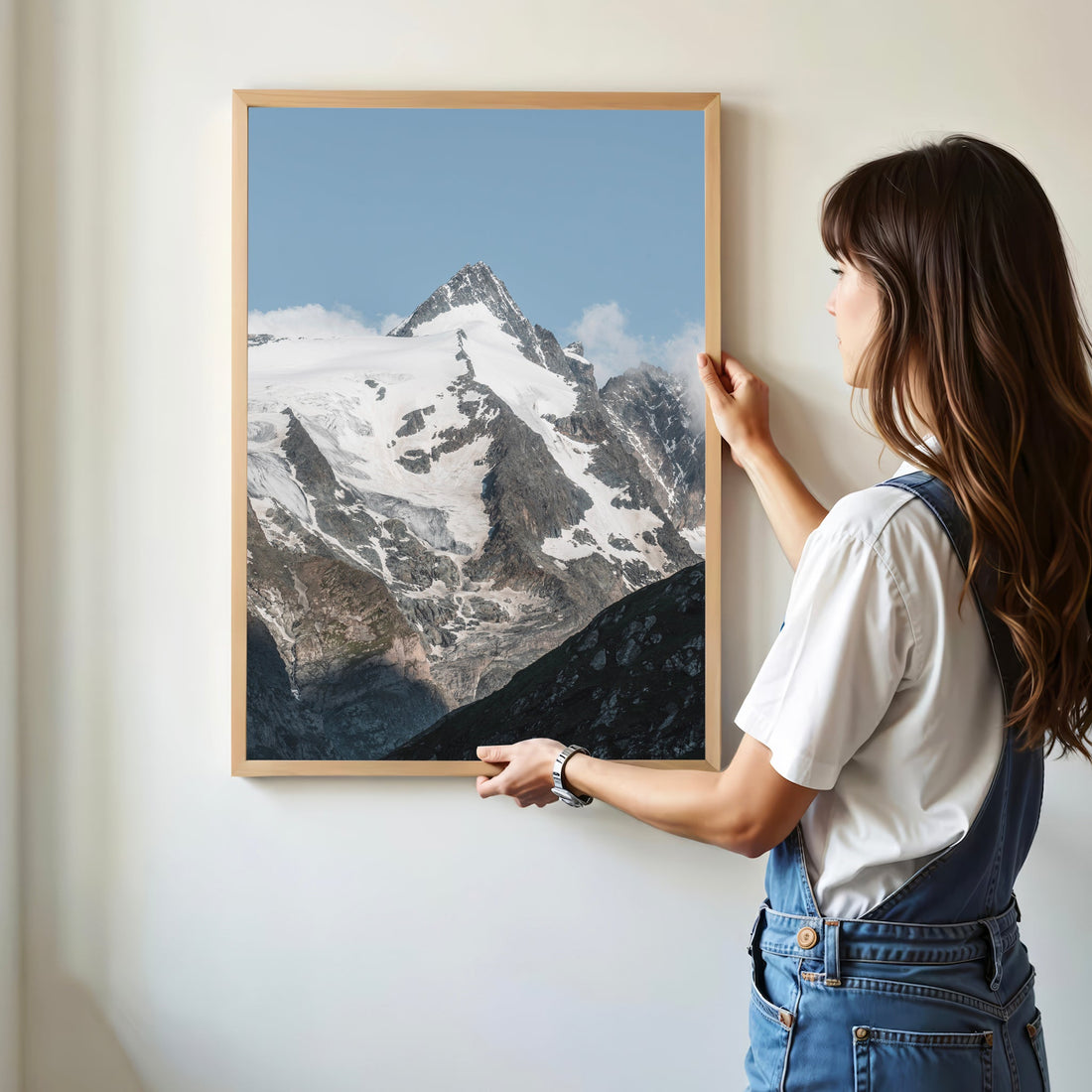 Woman hanging Grossglockner summit wall art in a light-filled interior.