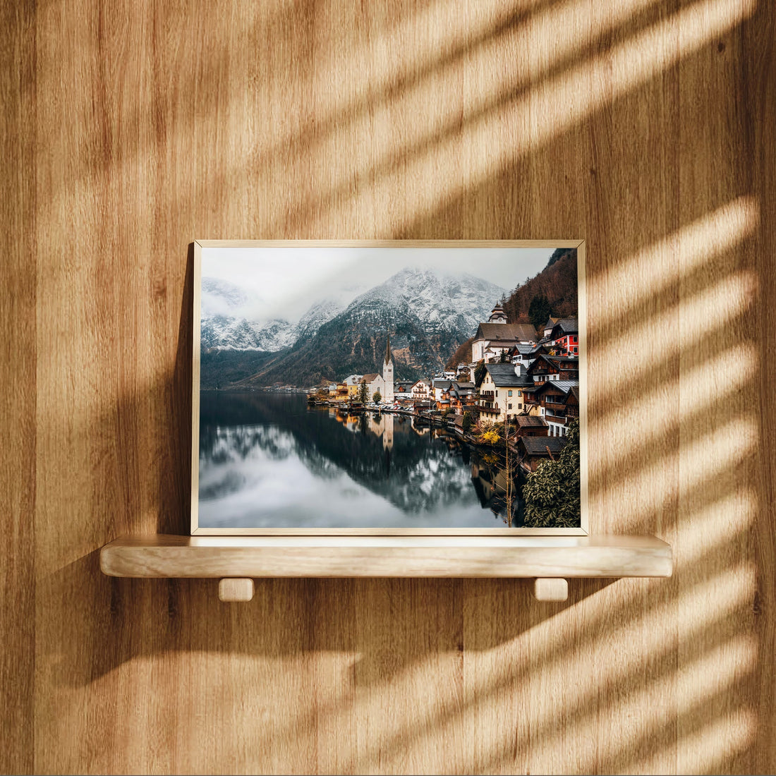 Framed Austrian landscape print of Hallstatt placed on a wooden shelf with natural light.