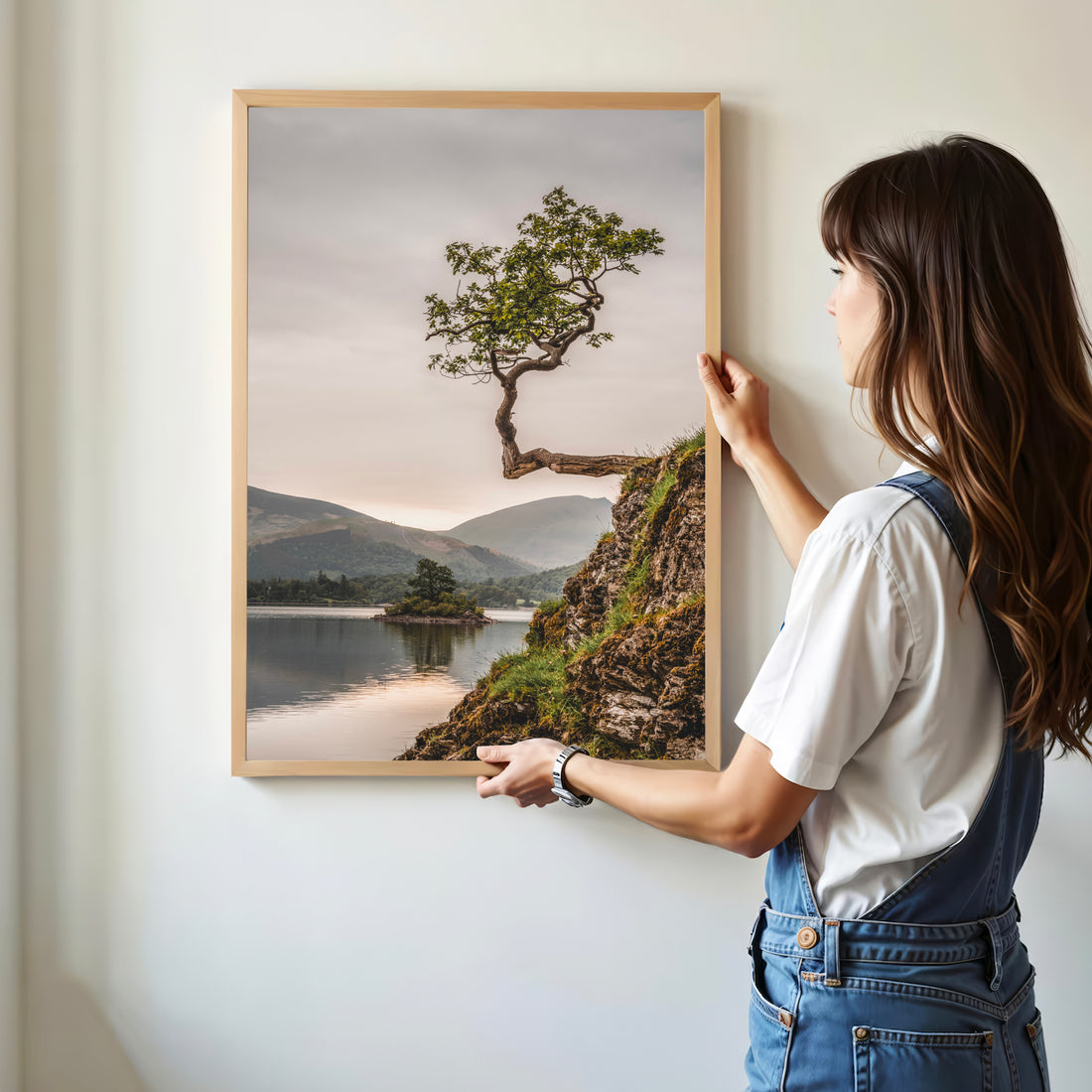 Woman hanging framed tree art on a white wall in a modern home