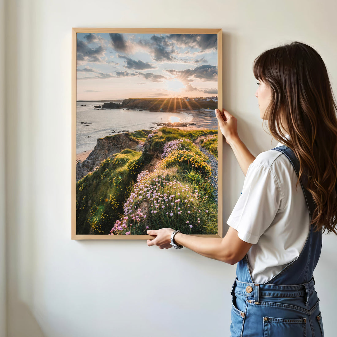 Woman holding a framed print of Annestown Beach at sunrise, with wild coastal flowers.