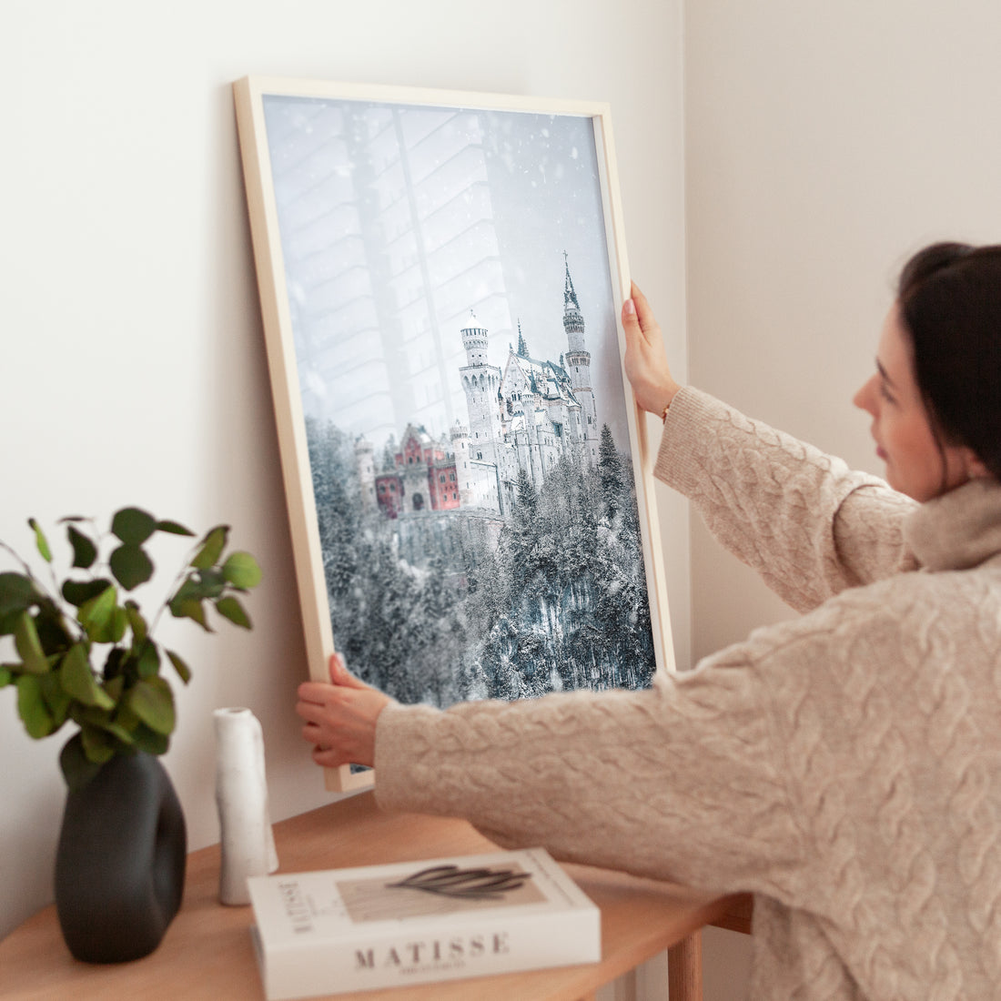 Close-up of person placing framed Neuschwanstein Castle photo on a modern dresser