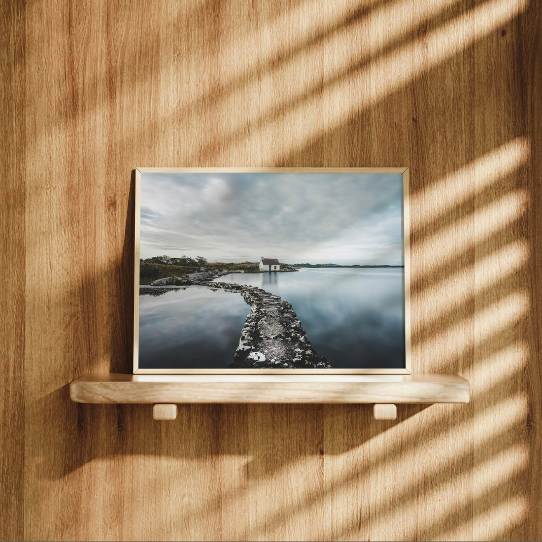 Fisherman’s cottage wall print on a wooden shelf with shadows cast across the frame.