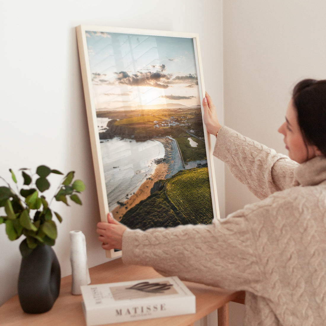Woman positioning an Annestown aerial print on wooden table next to books and vase