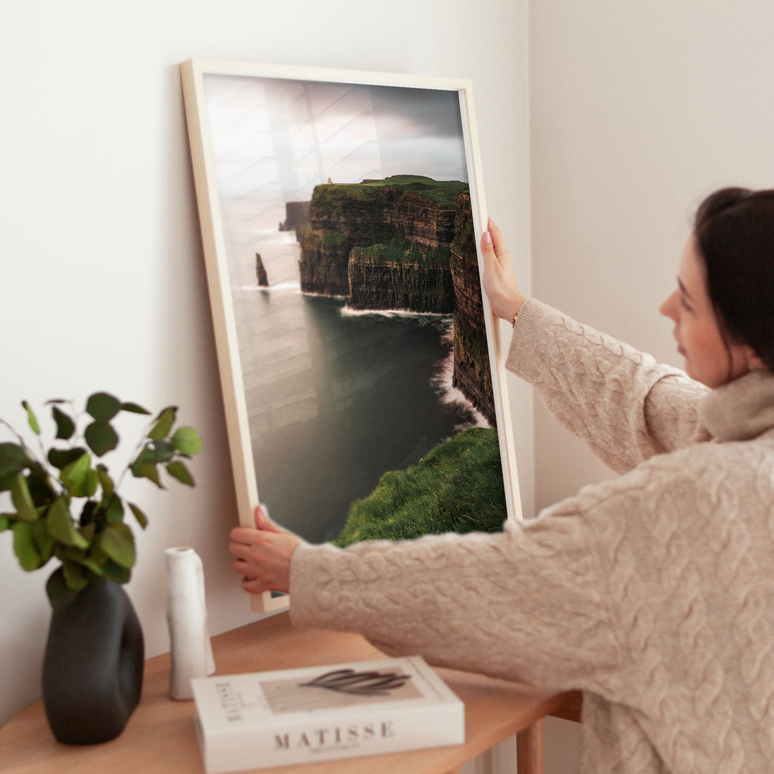 Woman styling a Cliffs of Moher print on a table with a Matisse book